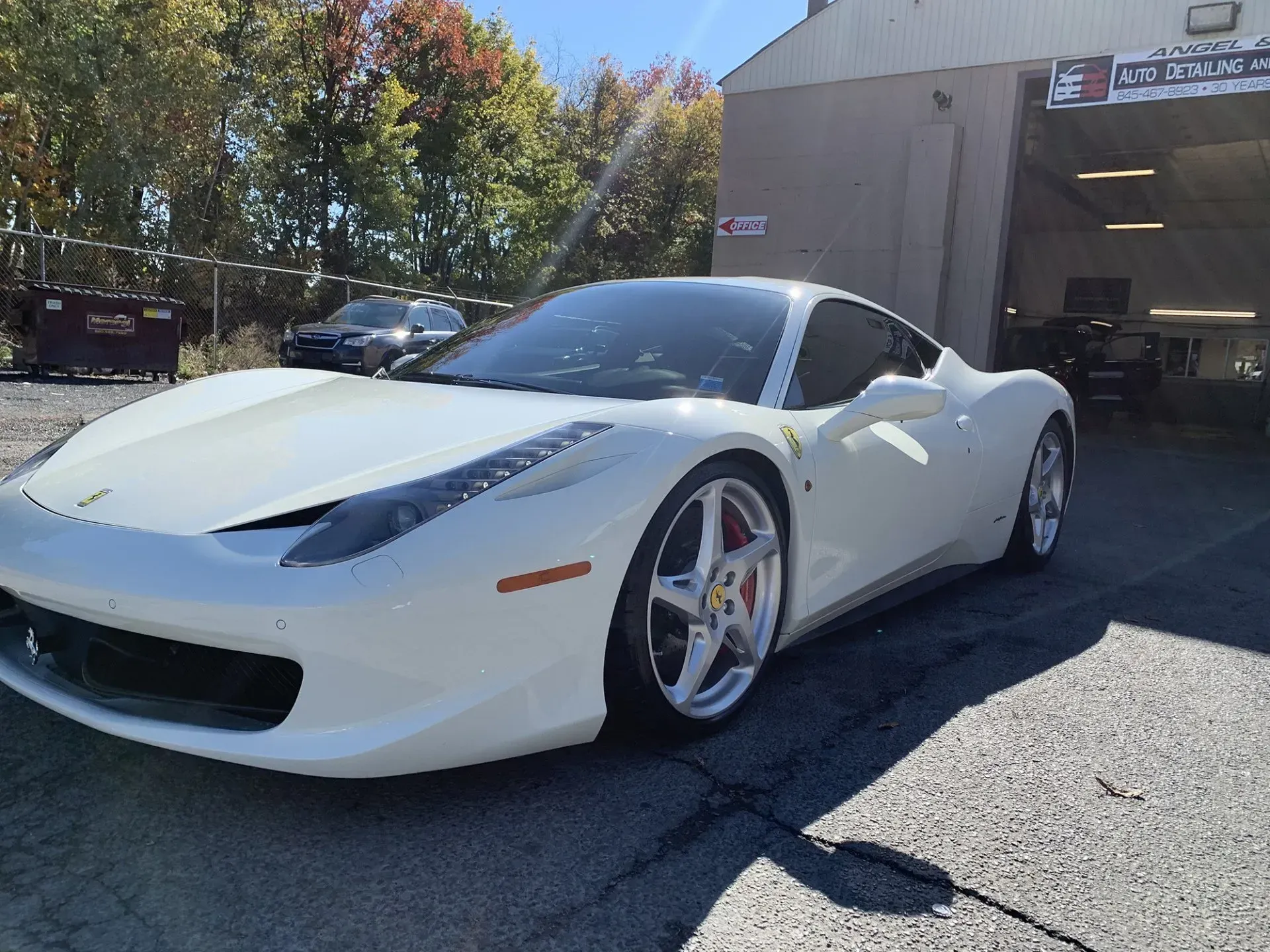 White Ferrari 458 Italia sports car parked outside a garage on a sunny day.