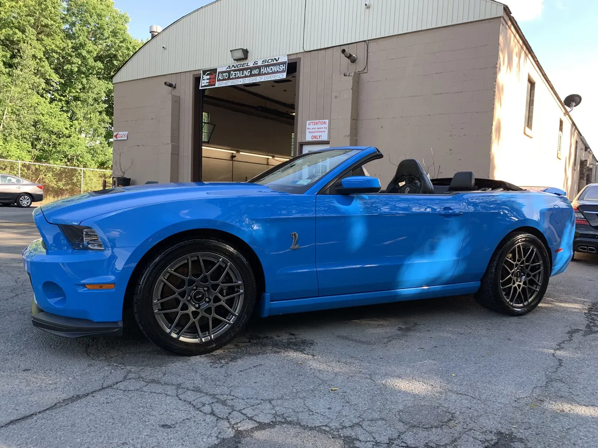 Blue Ford Mustang convertible parked outside a garage with a dark roof.
