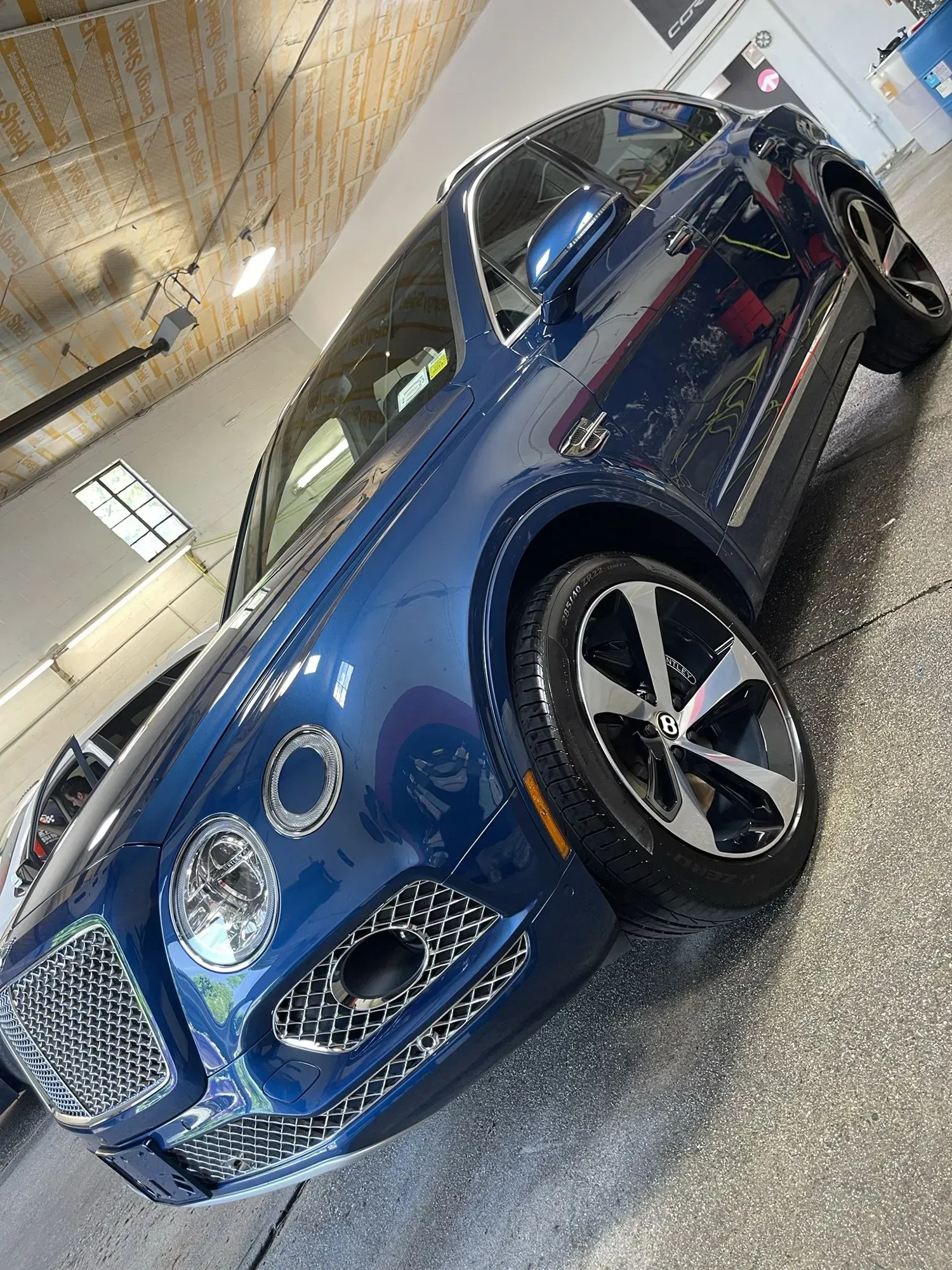 Blue Bentley SUV parked indoors with reflective flooring.