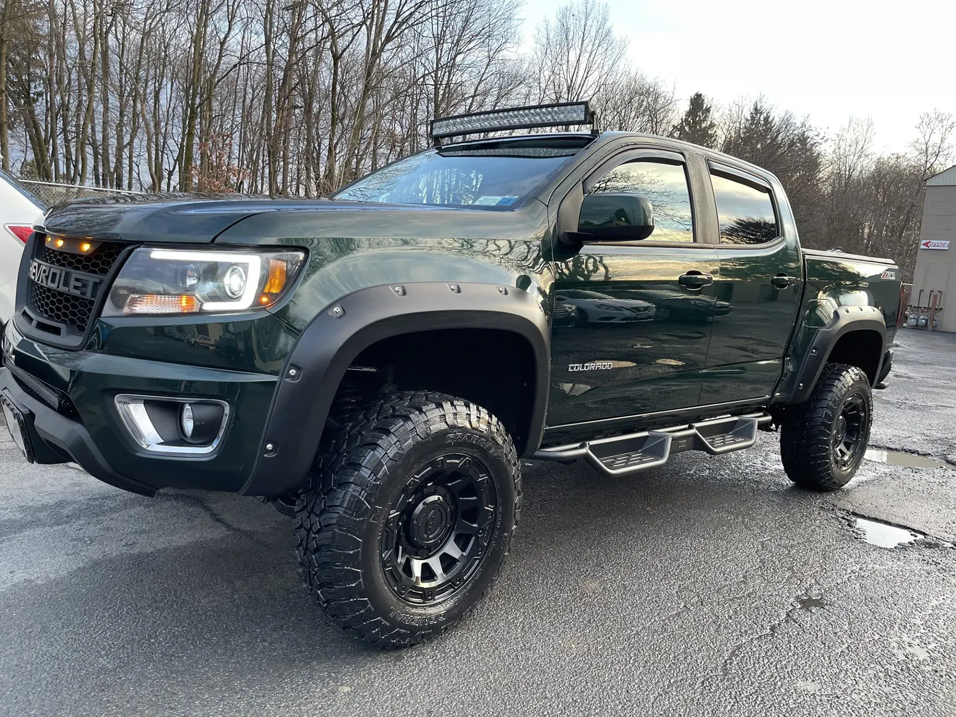 Dark green lifted Chevrolet Colorado pickup truck with black accents, light bar, and off-road tires.