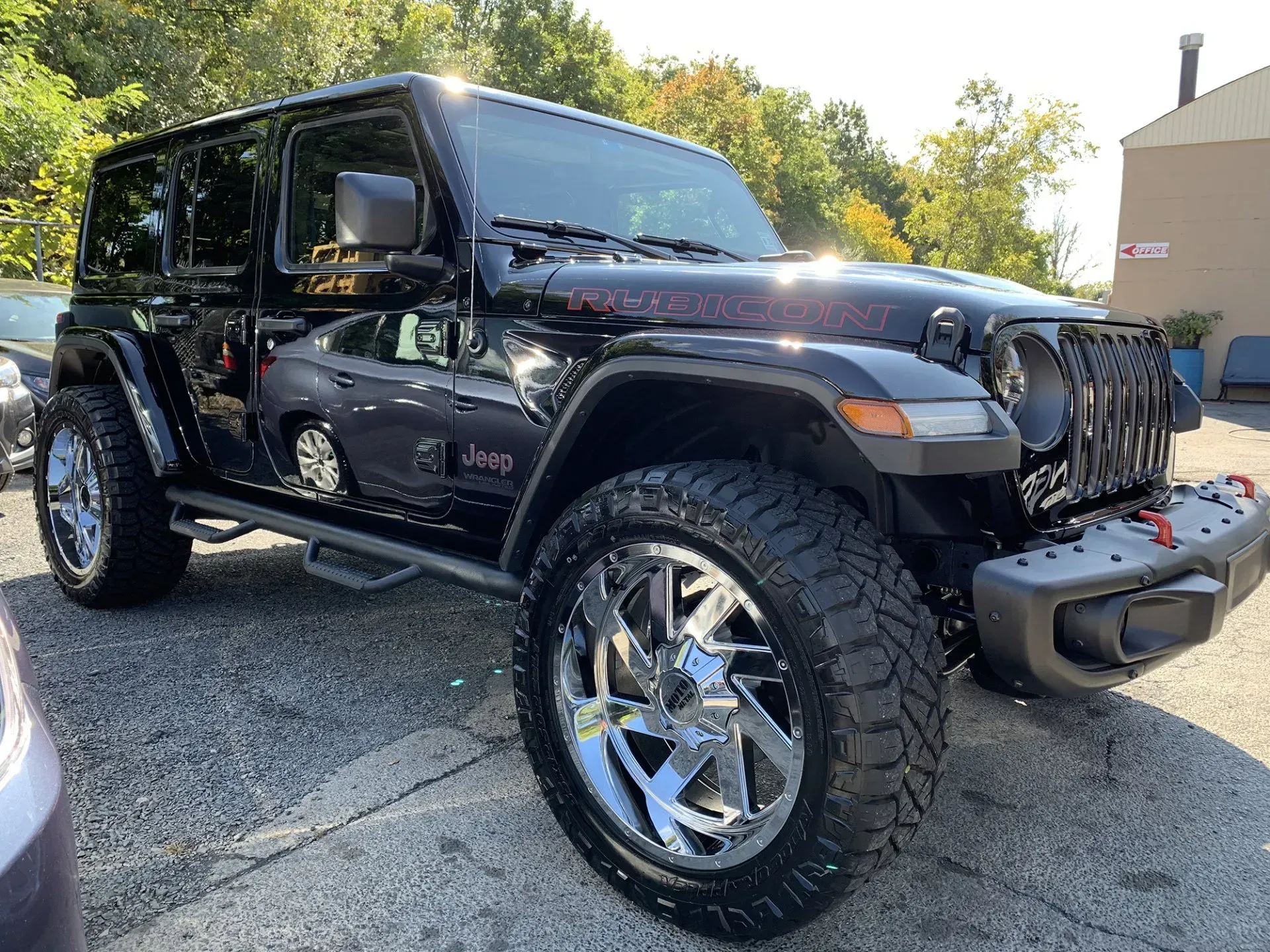 Black Jeep Wrangler with chrome wheels parked outside on a sunny day.
