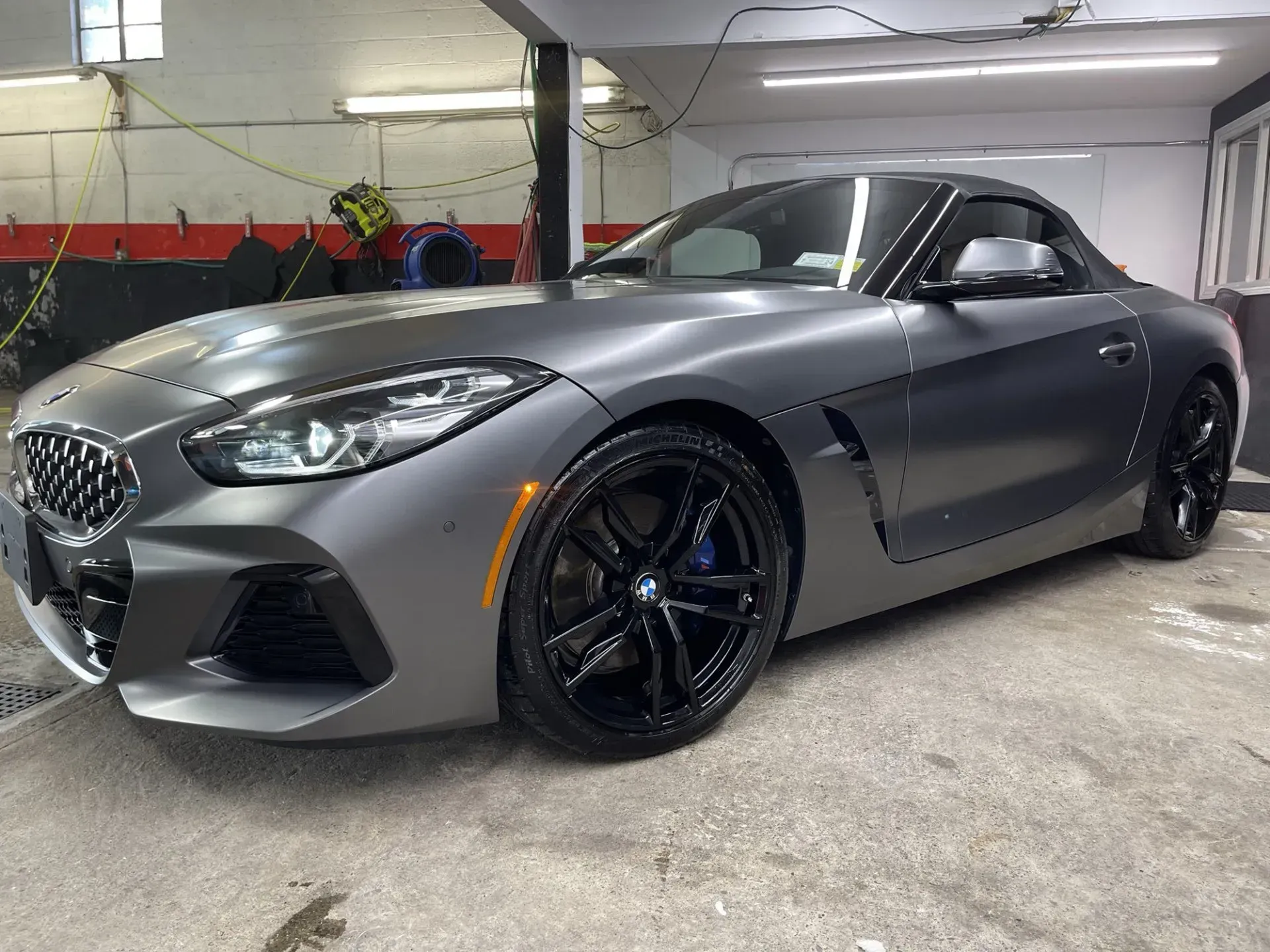 Gray BMW Z4 convertible parked in a garage with black wheels.