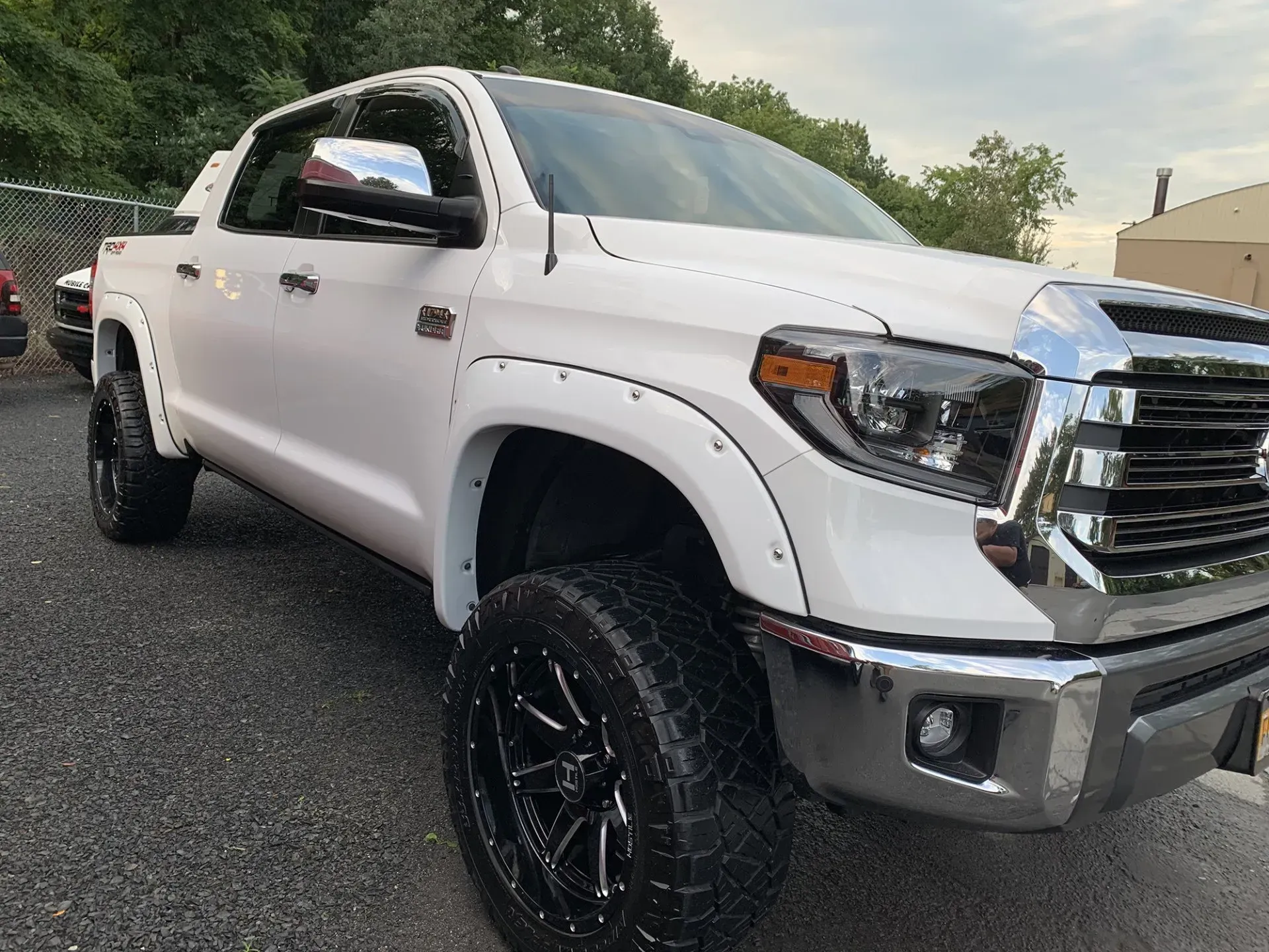 White Toyota Tundra truck with black rims parked on asphalt, near a fence.