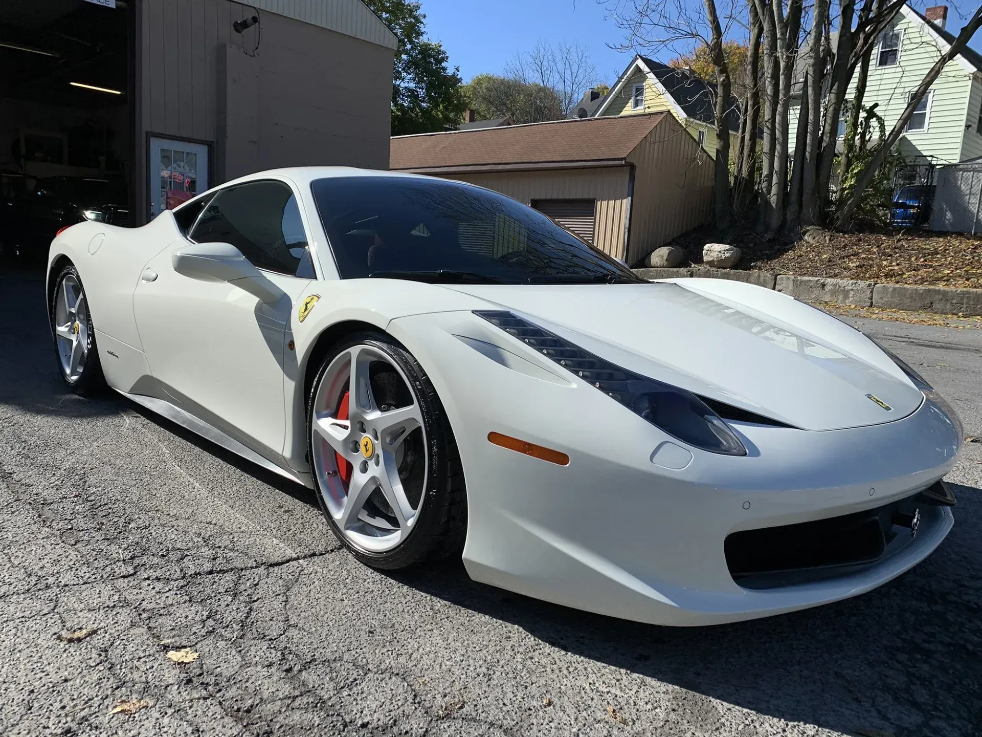 White Ferrari sports car parked on a city street, red brake calipers visible.