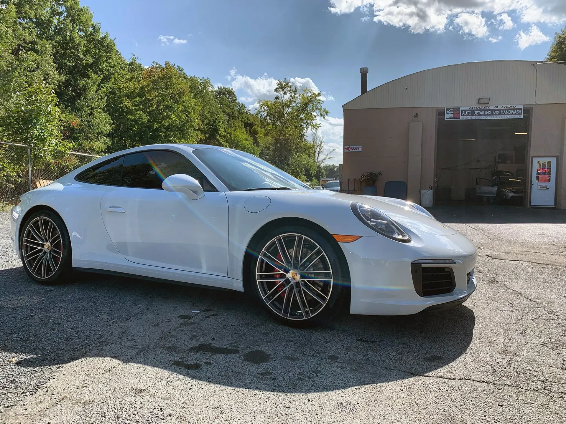 White Porsche parked in front of a garage on a sunny day.