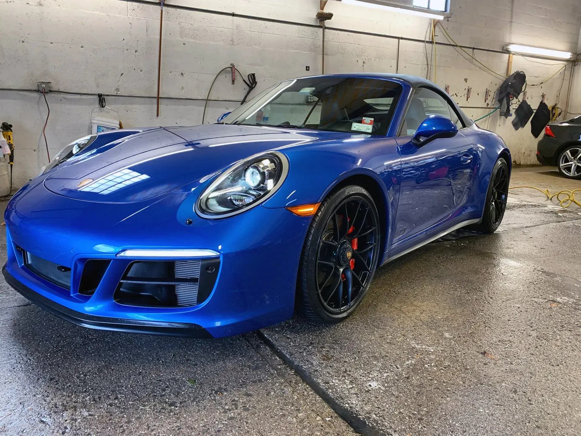 Blue Porsche sports car in a car wash bay; black wheels and red brake calipers.