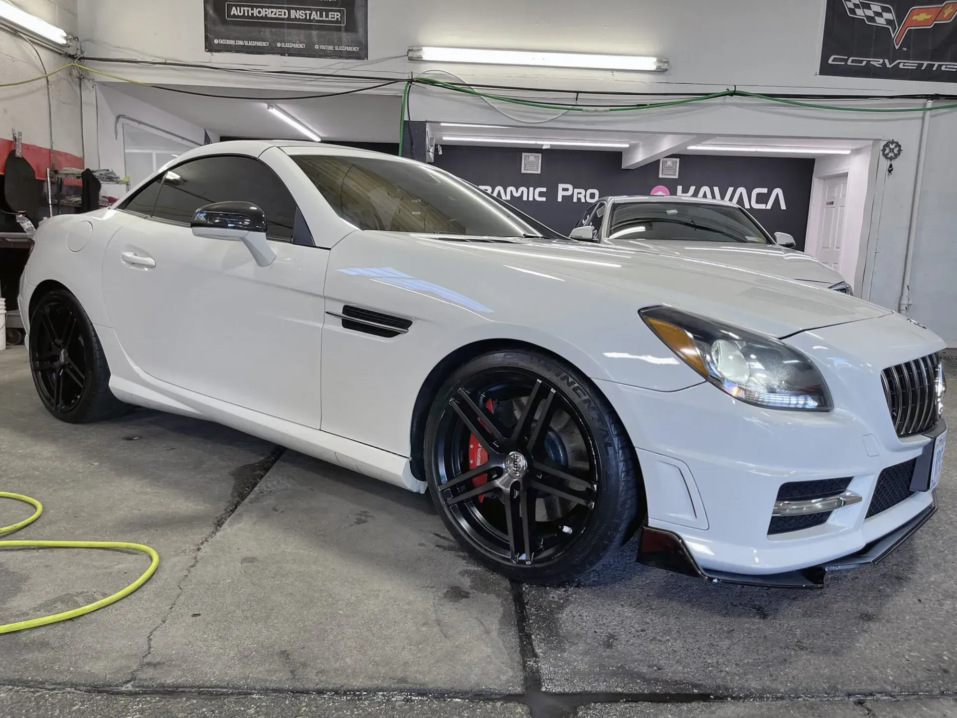White Mercedes SLK convertible with black rims parked inside a garage.