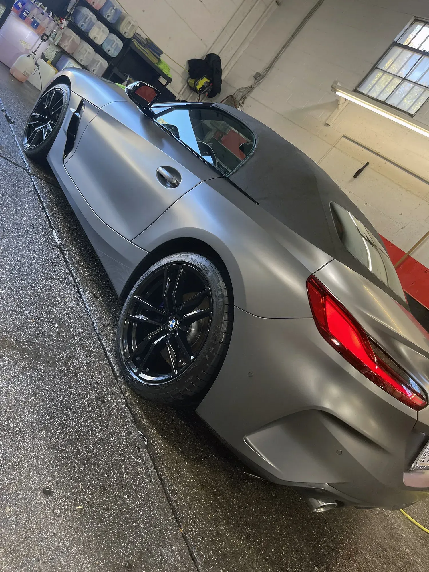 Gray convertible car with black wheels in a car wash setting.