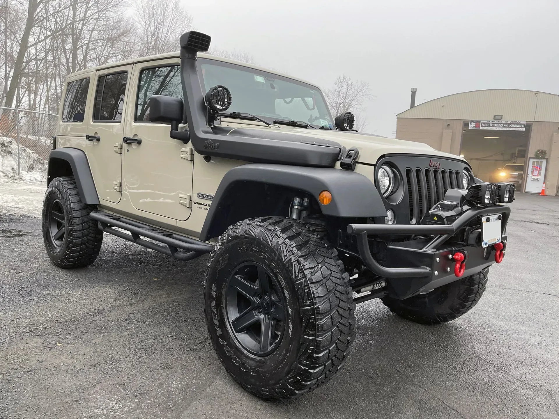 Tan Jeep Wrangler with black accents, snorkel, and large off-road tires parked on a gravel lot.