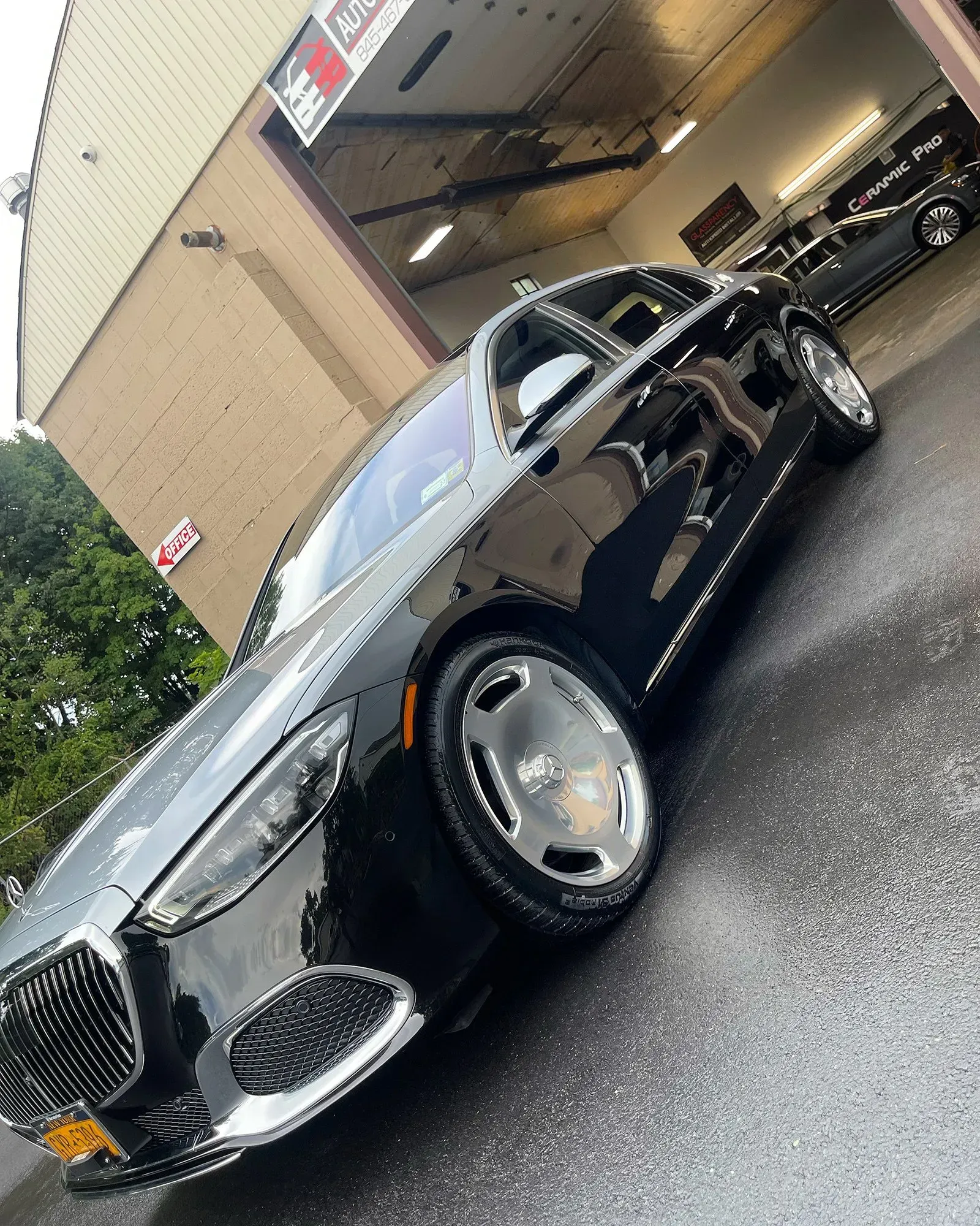 Black Mercedes Maybach sedan parked outside a car wash with wet pavement.