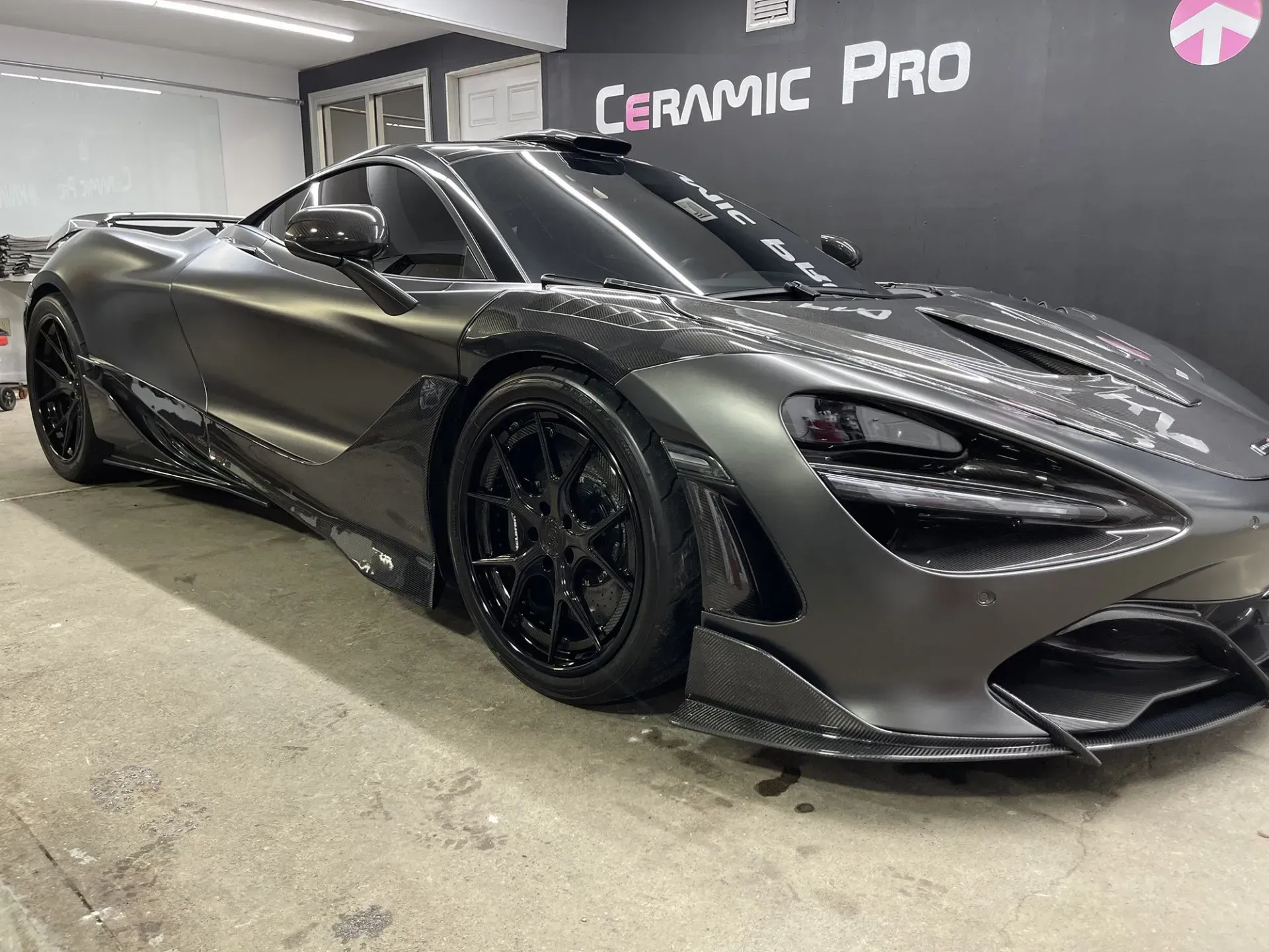 Dark gray McLaren sports car with black wheels, in a garage with