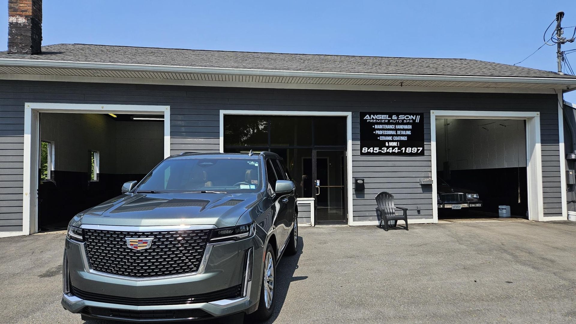 Gray Cadillac SUV parked in front of a gray building with open garage doors.