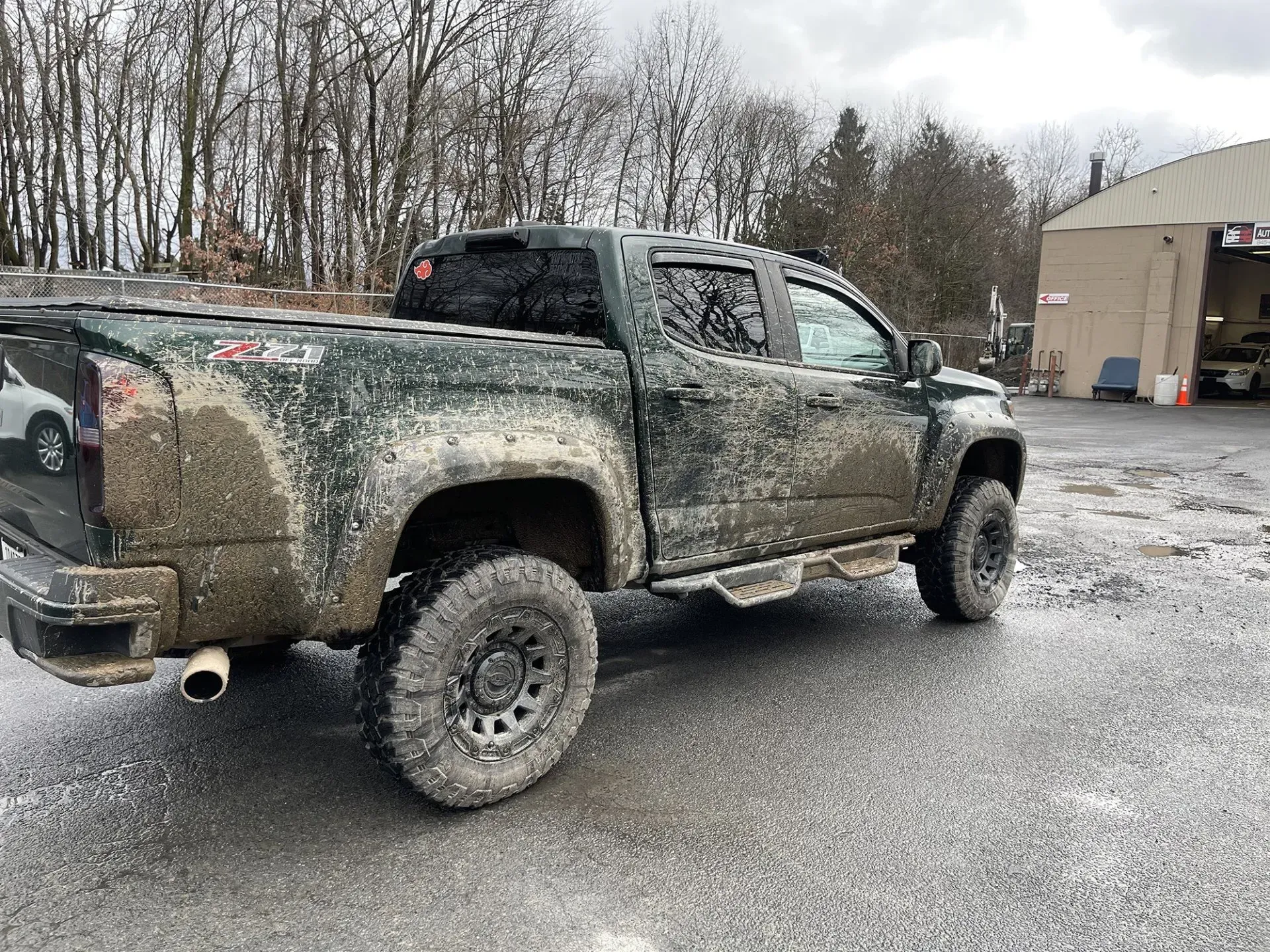 Mud-covered Chevy pickup truck with black wheels parked on a wet paved area.