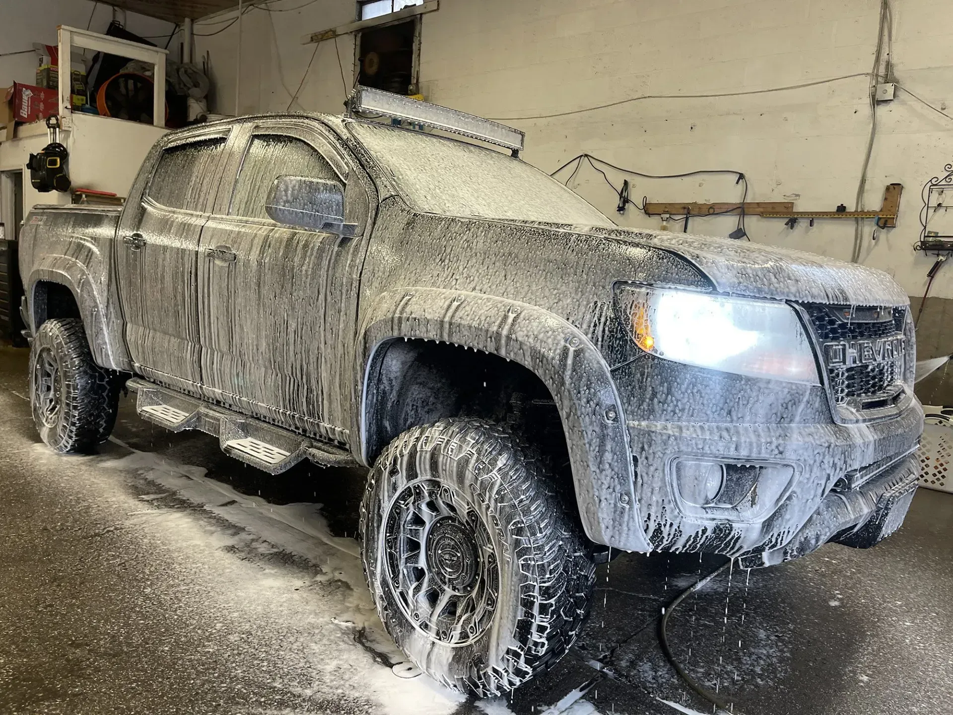 Black pickup truck covered in foam, being washed in a garage.