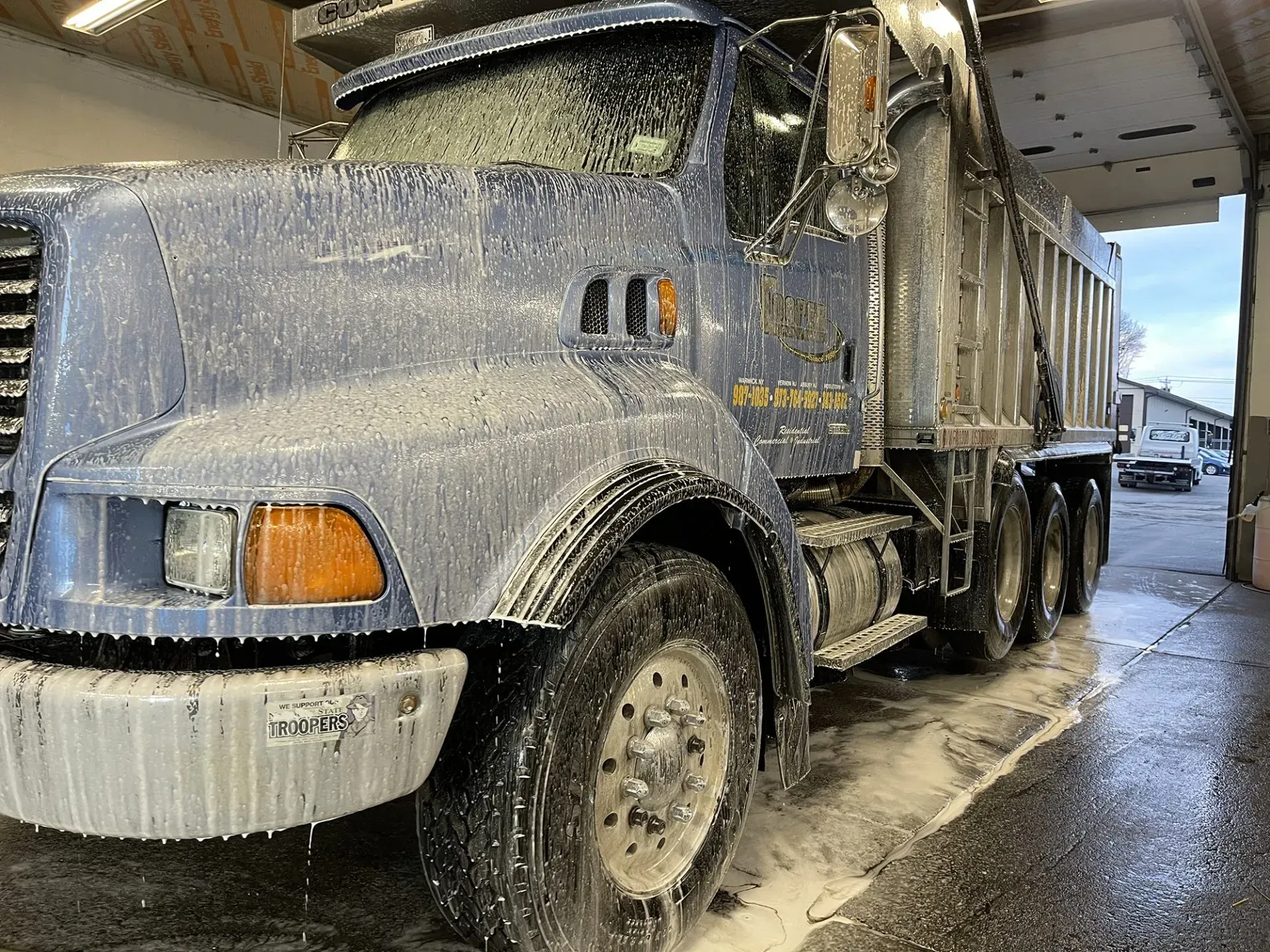 Blue dump truck covered in foam at a car wash.