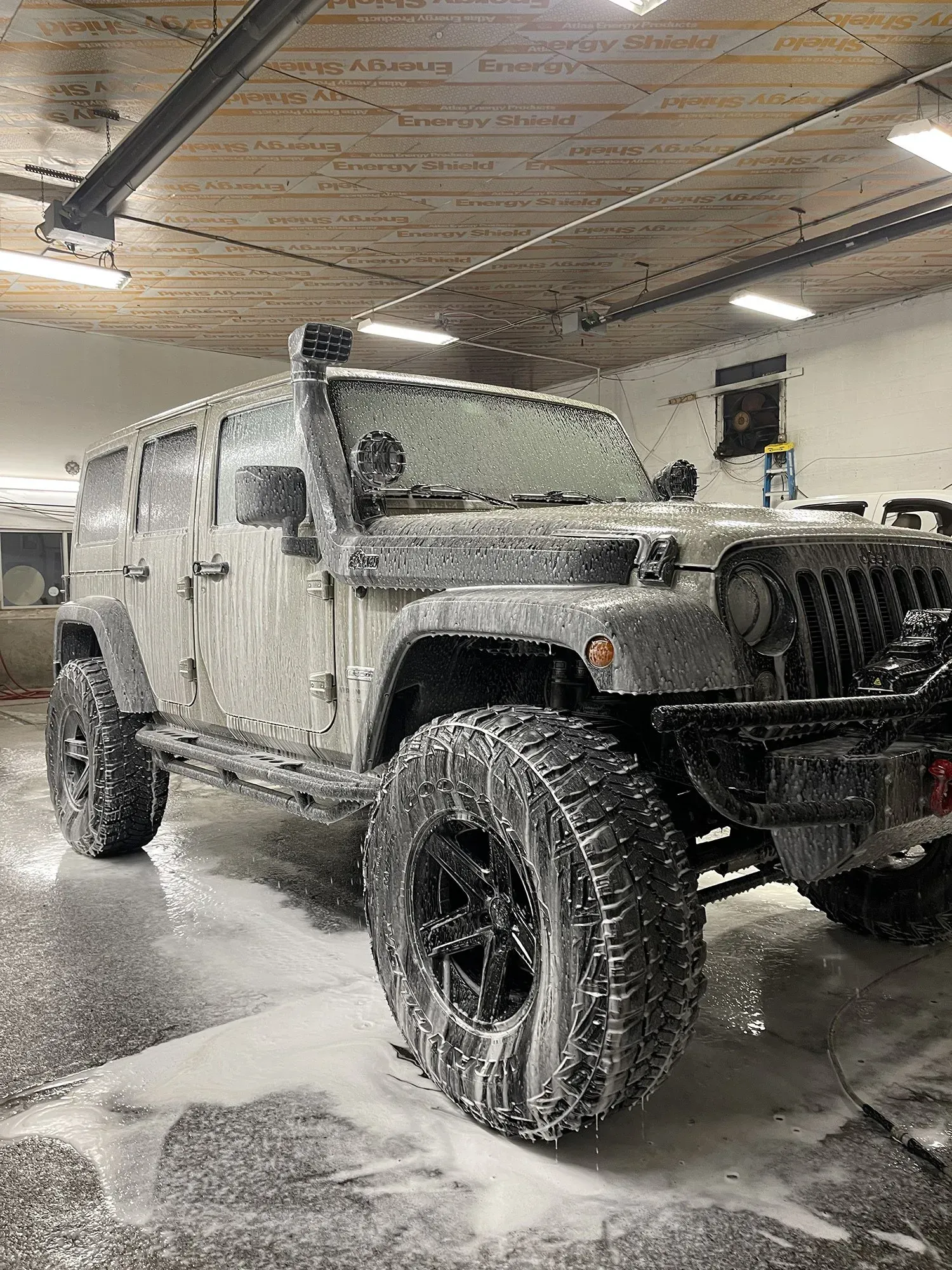 A Jeep Wrangler covered in soap suds in a garage, ready for washing.