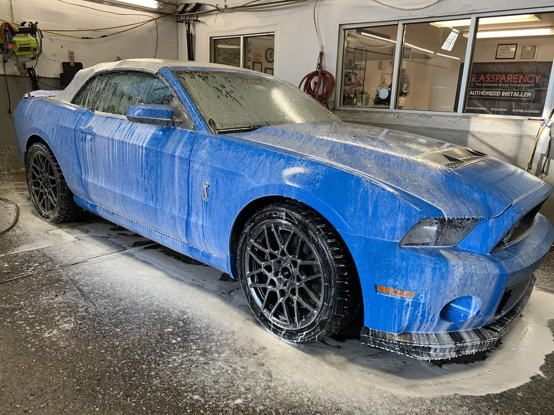 Blue Ford Mustang convertible covered in soap at a car wash.