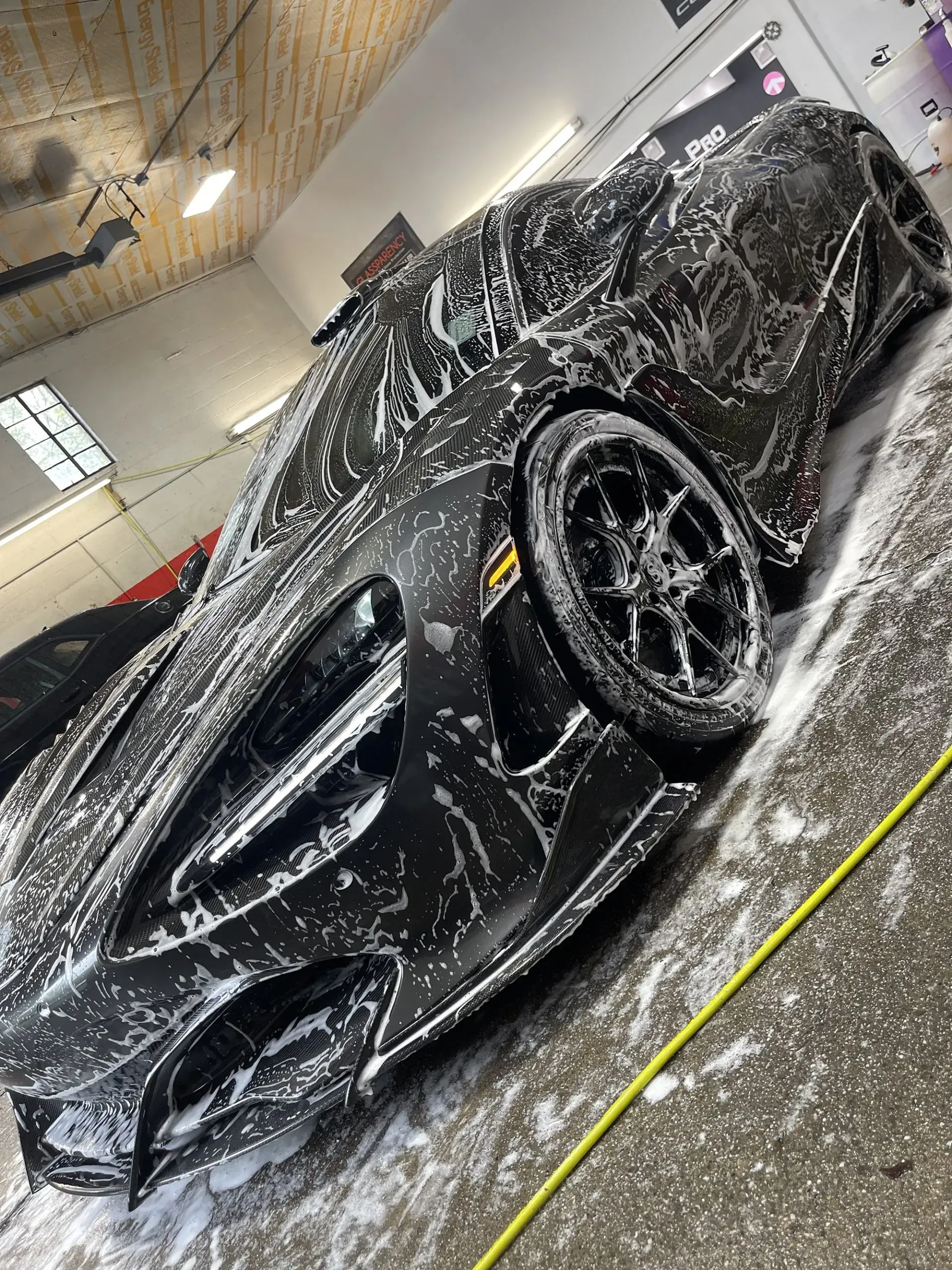 Black sports car covered in white soap, being washed indoors.