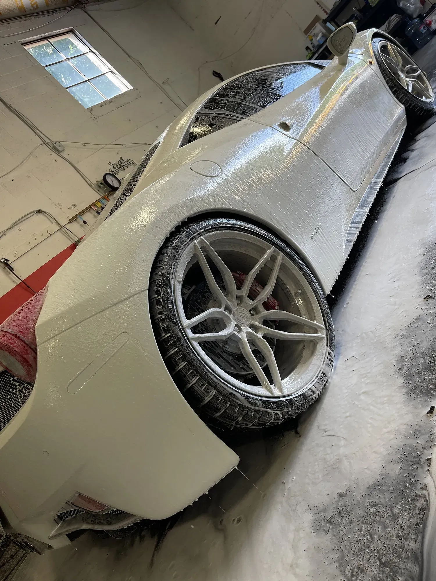 White sports car covered in soapy foam, in a car wash bay.