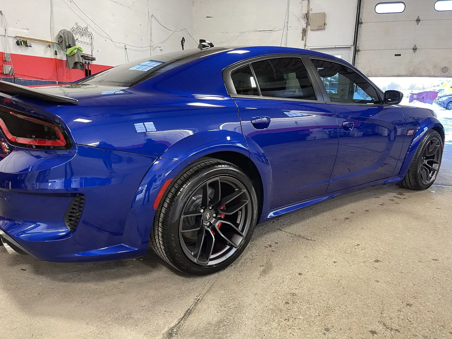 Blue Dodge Charger, black rims, parked inside a garage, side view.