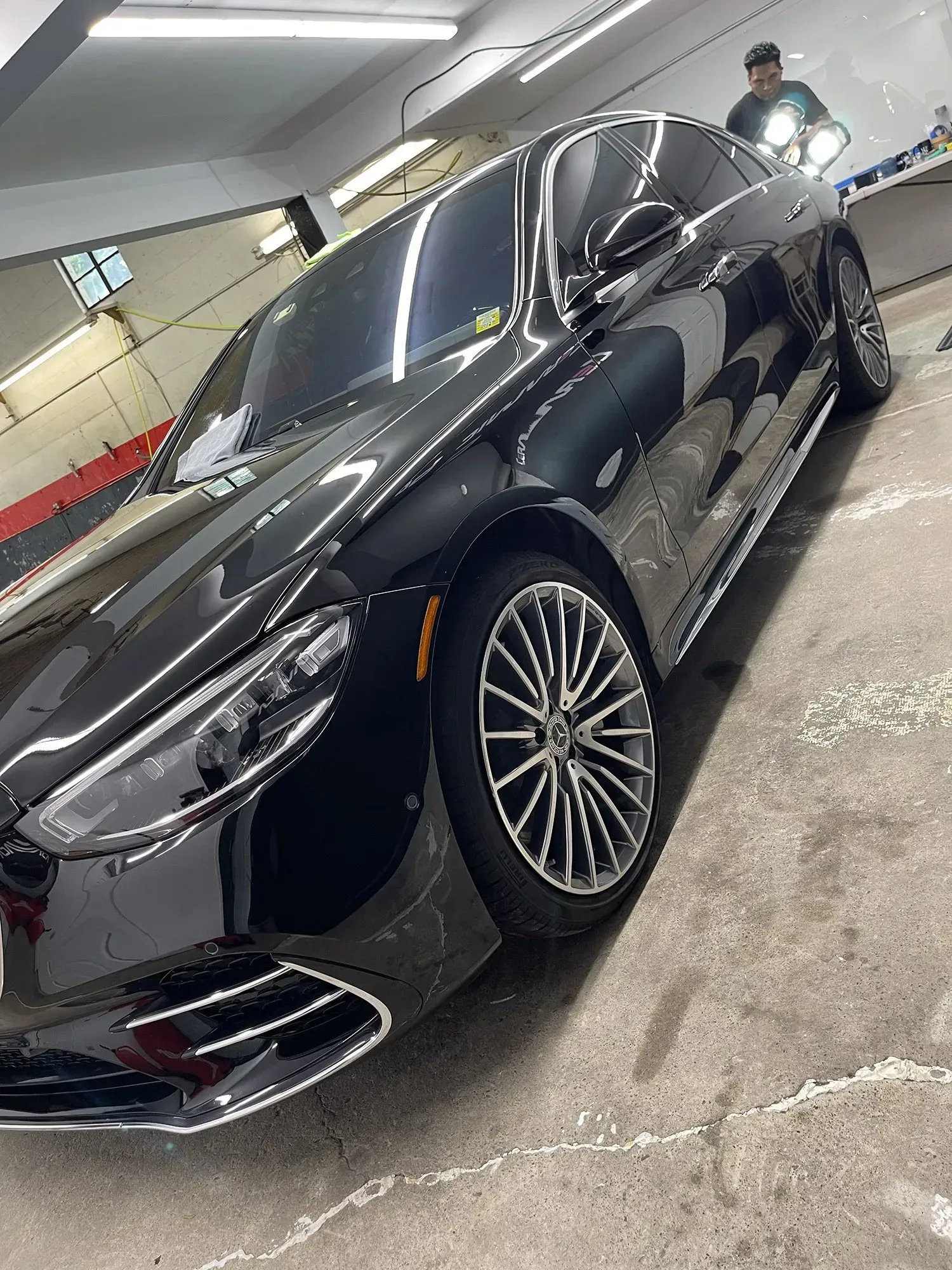 Black Mercedes sedan parked inside a garage, person on a scooter in the background.
