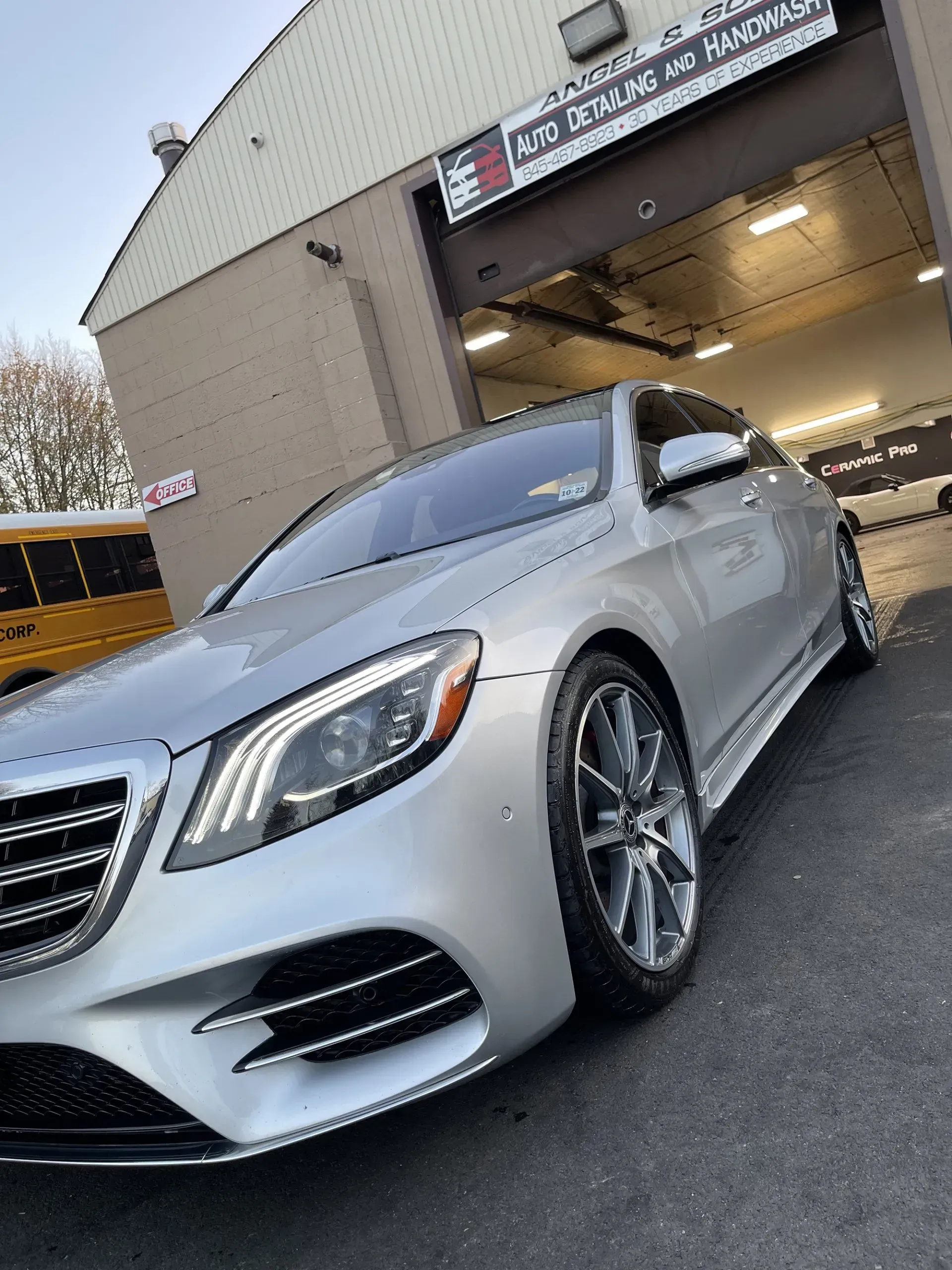 Silver Mercedes sedan parked in front of an auto repair shop with a school bus visible in the background.