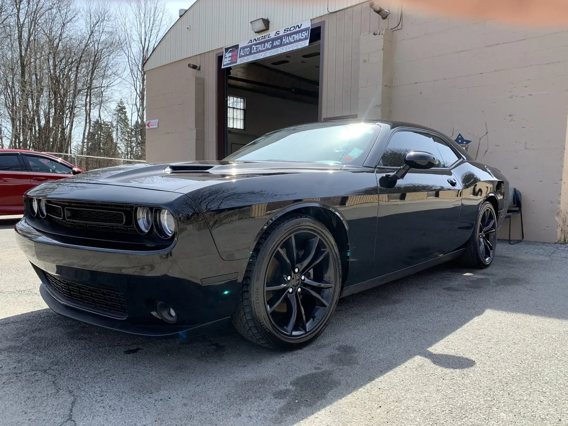Black Dodge Challenger parked outside a shop with black rims, hood scoop and tinted windows.