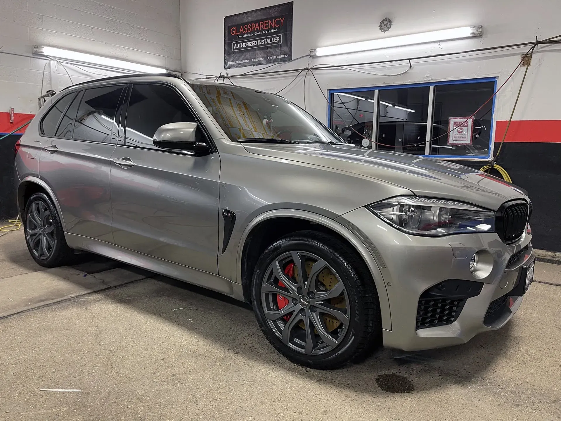 Silver BMW X5 M SUV with tinted windows, red brake calipers, and black rims.