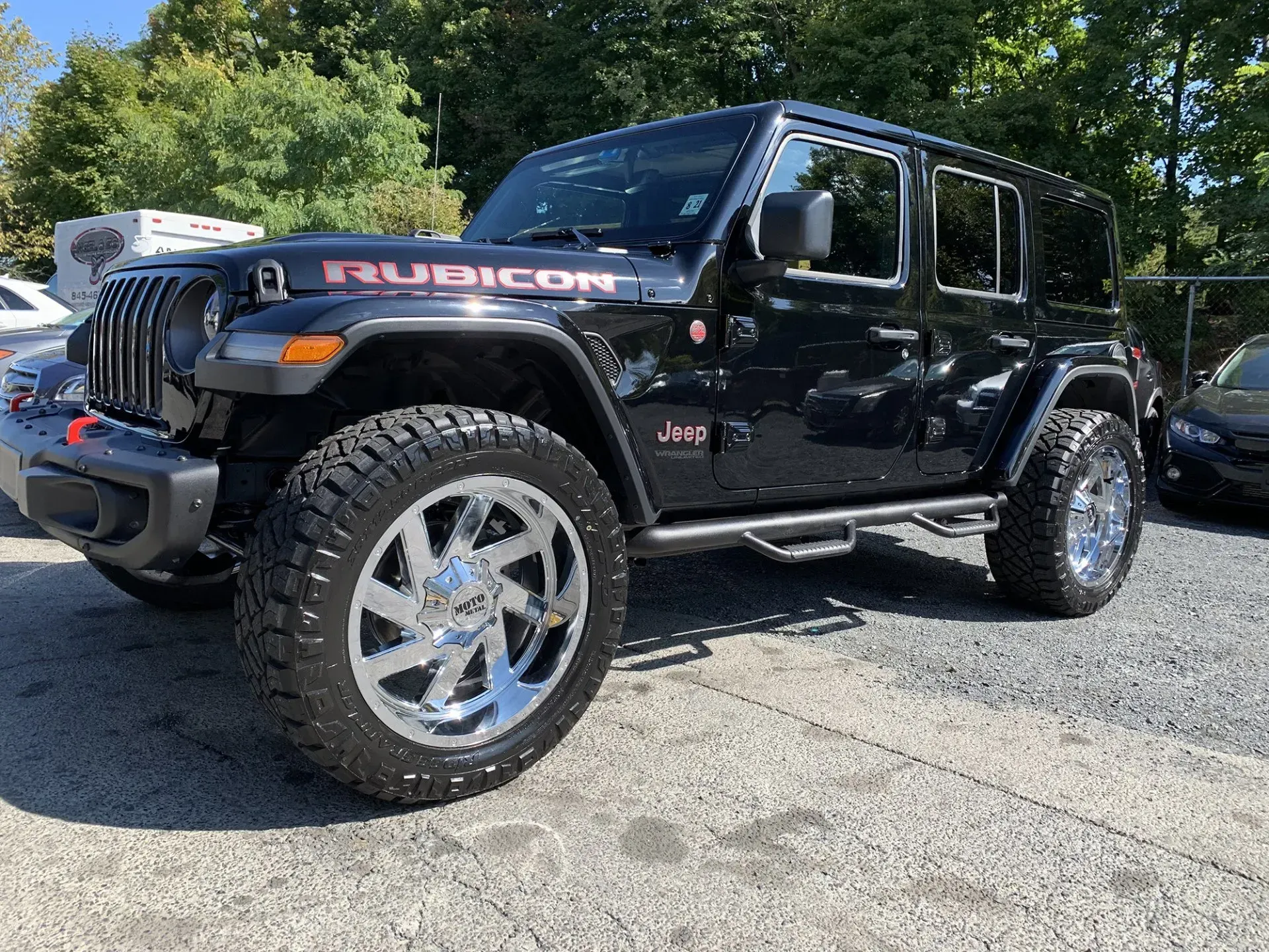 Black Jeep Rubicon with chrome wheels parked outside on a sunny day.