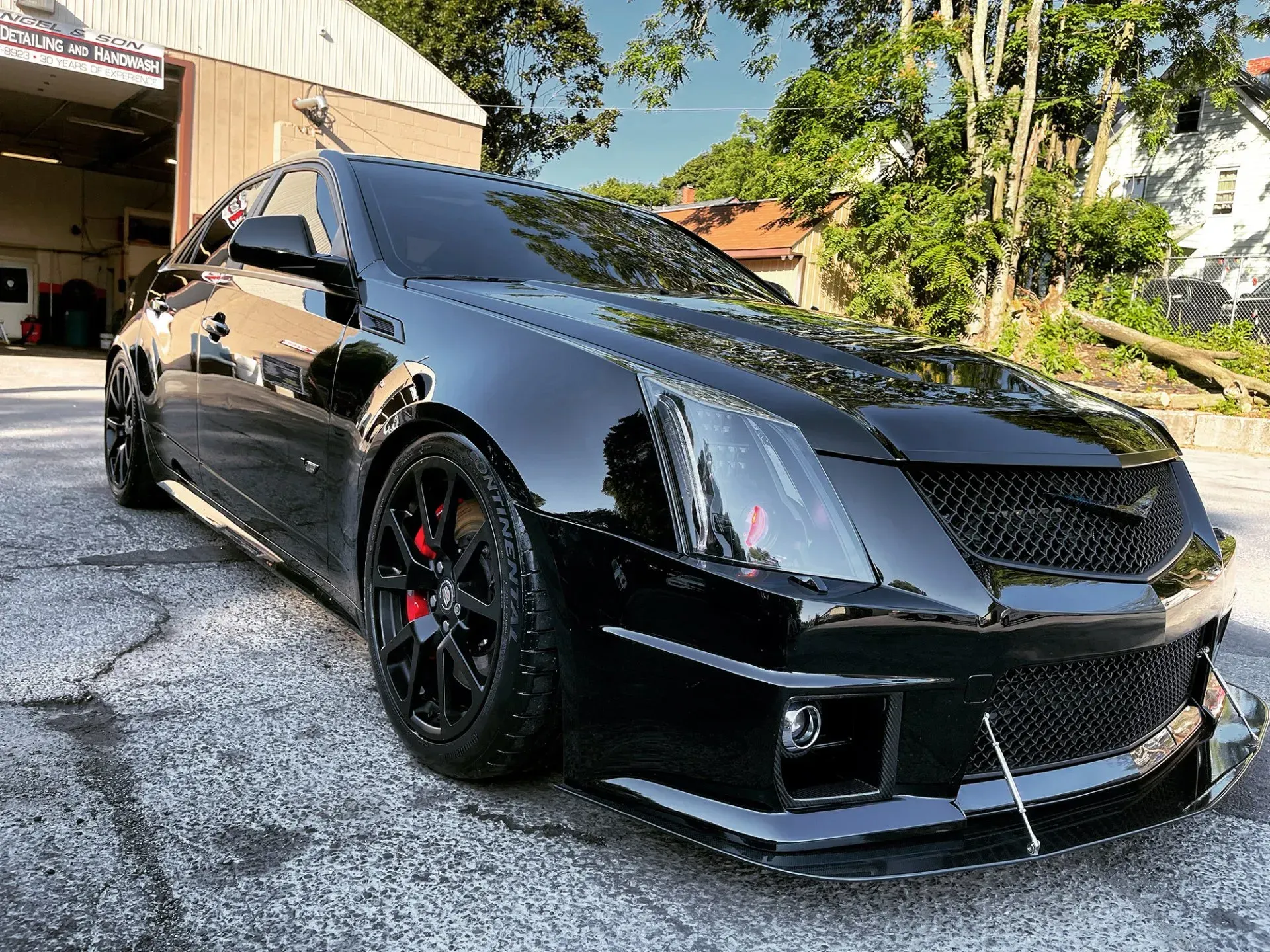 Black Cadillac CTS-V with blacked-out grill and wheels, red brake calipers. Parked outside a building on a sunny day.