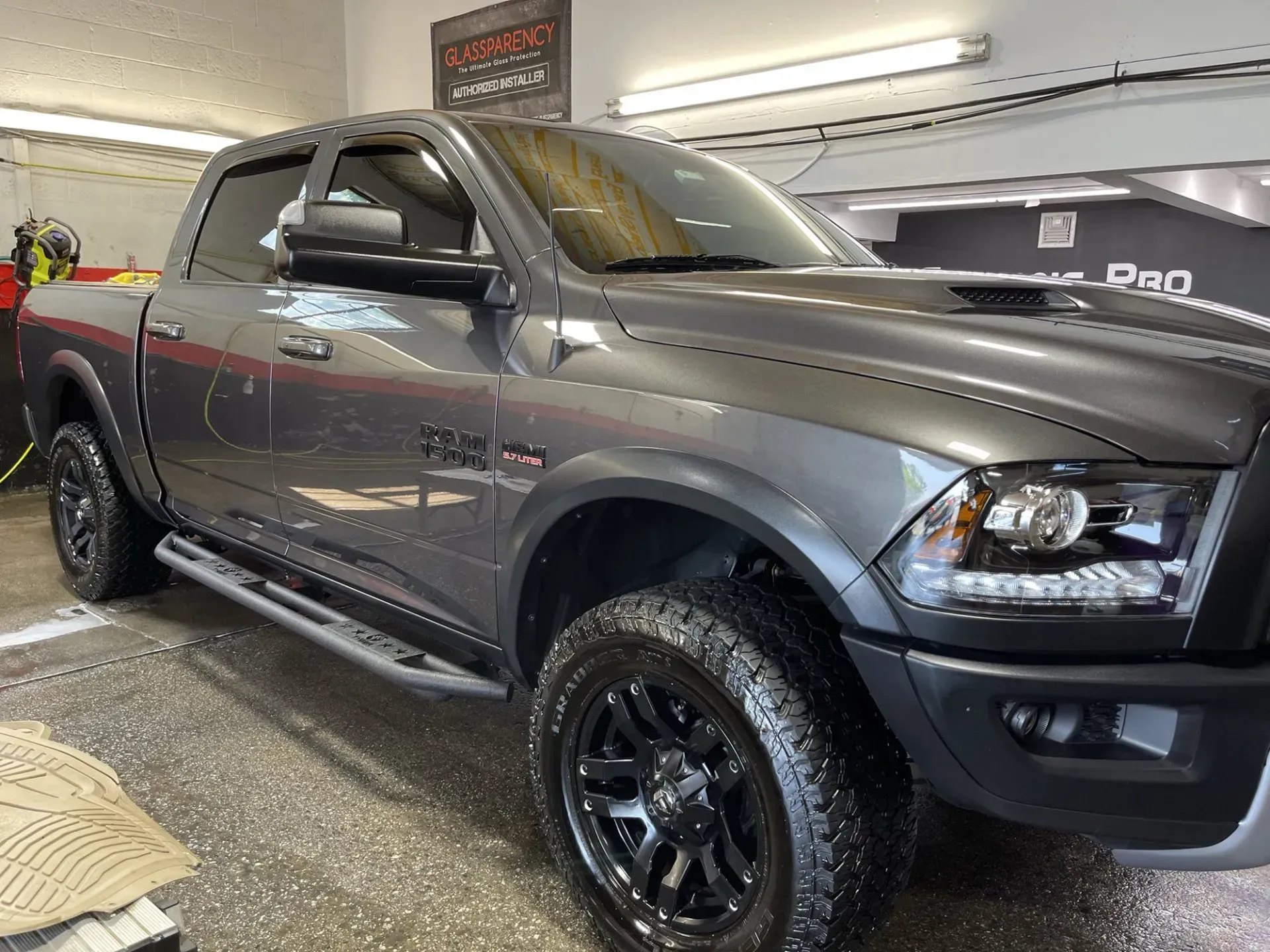 Gray Dodge Ram truck inside a shop, black wheels, side steps, tinted windows.