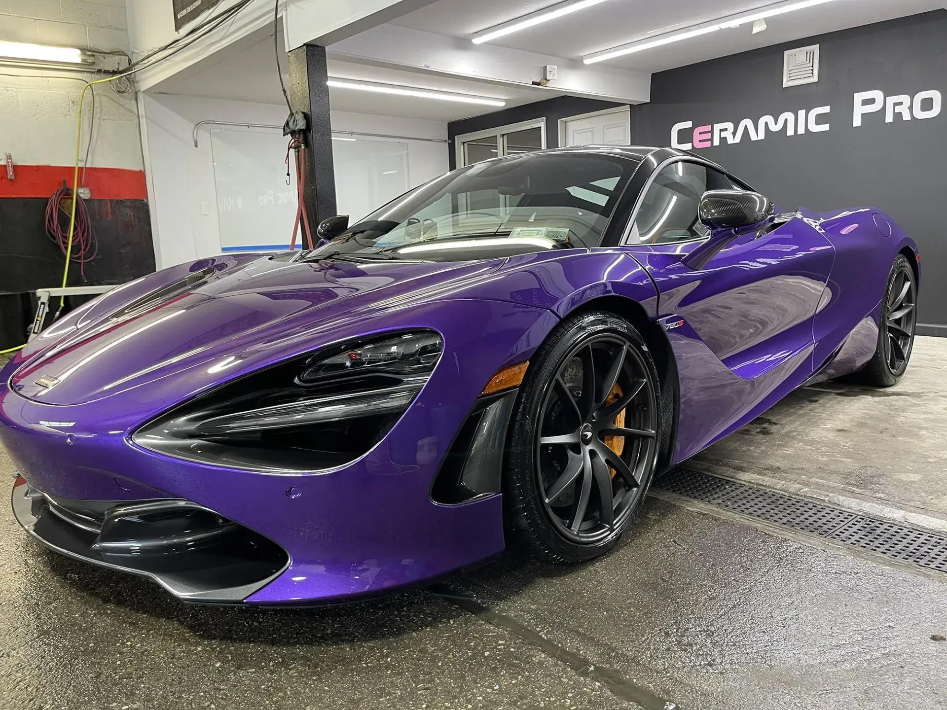 Purple McLaren sports car in a car wash bay, with orange brake calipers and black wheels.