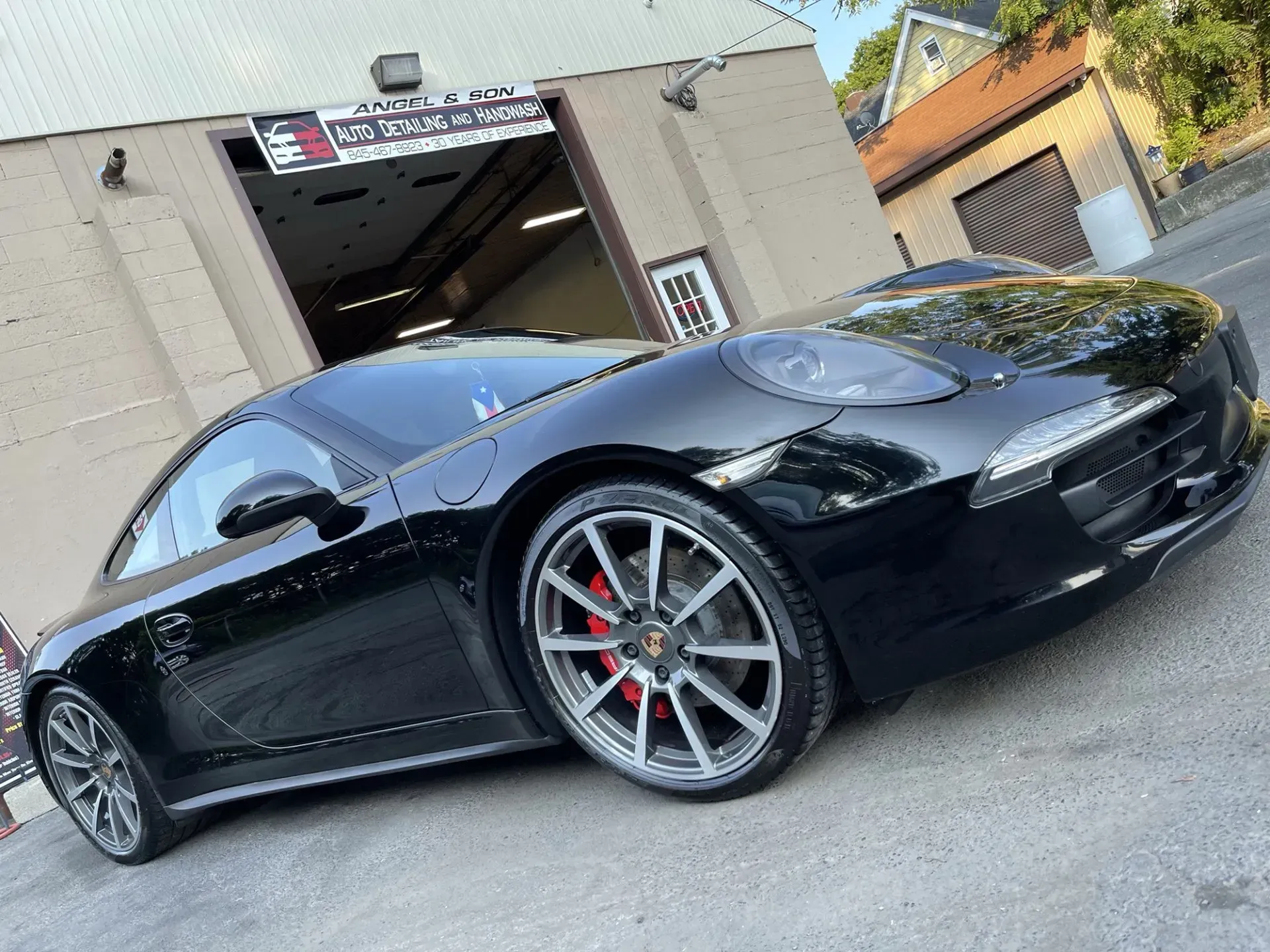 Black Porsche sports car parked outside a garage with red brake calipers.