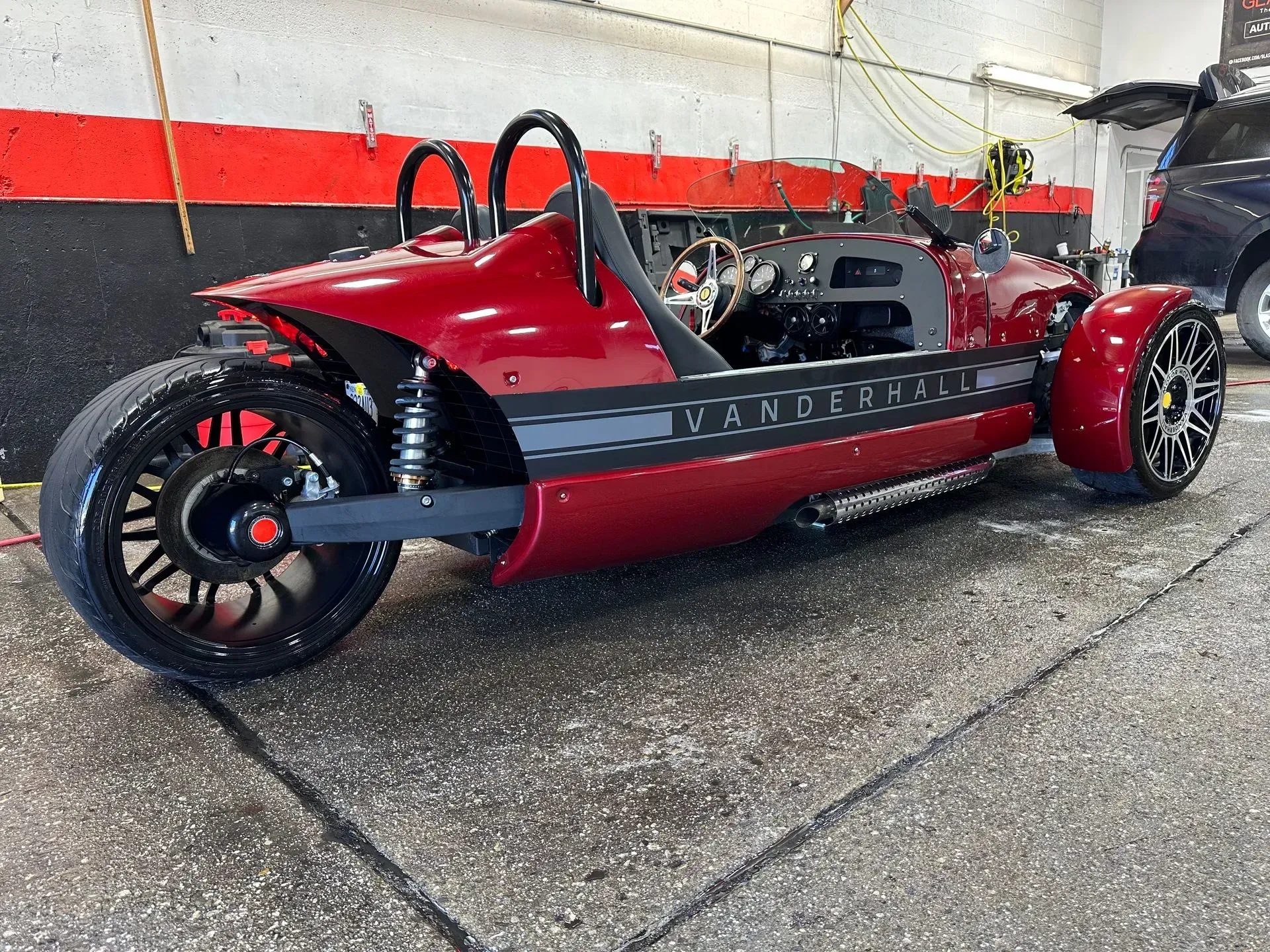 A maroon Vanderhall three-wheeler parked in a garage, black accents, wet pavement.