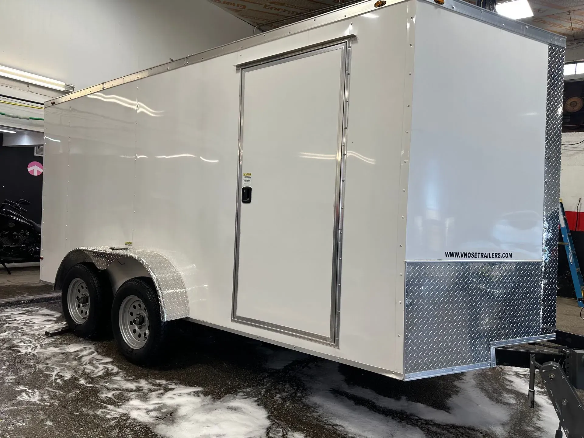 White enclosed cargo trailer with a silver diamond plate front, in a wash bay.