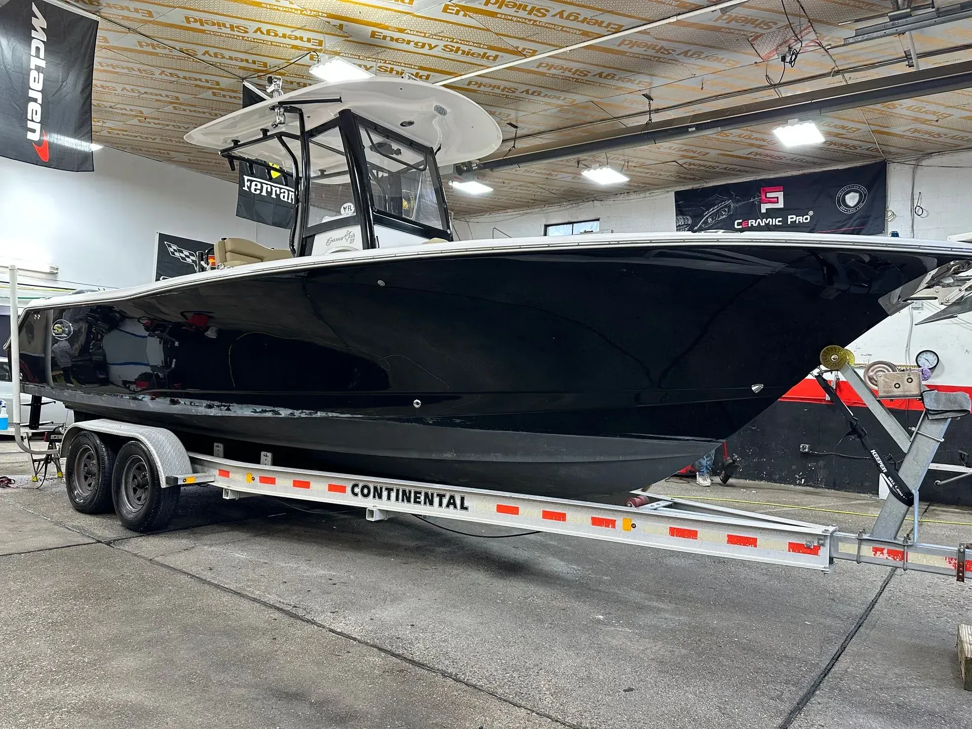 Black and white boat on a trailer in a garage, with white T-top and Continental trailer.
