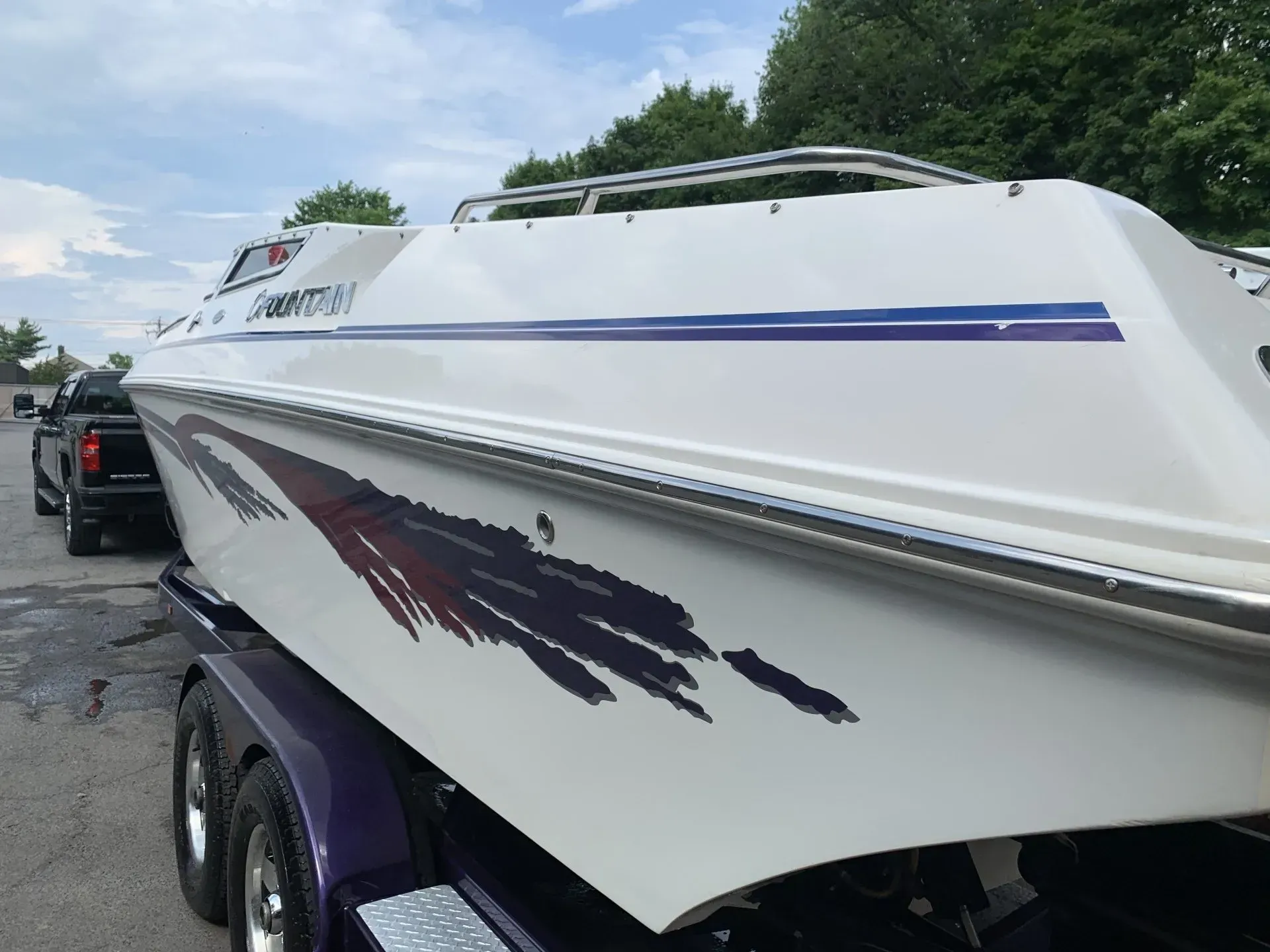 White speedboat on a trailer with a purple and red graphic, parked near a truck.