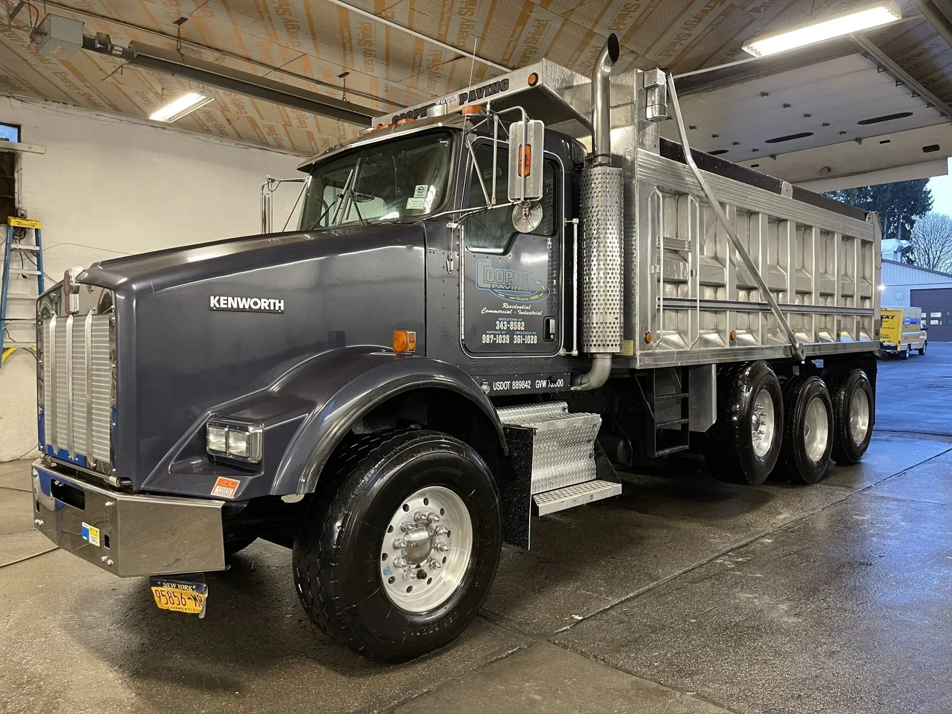 Dark blue Kenworth dump truck parked indoors, wet from washing.