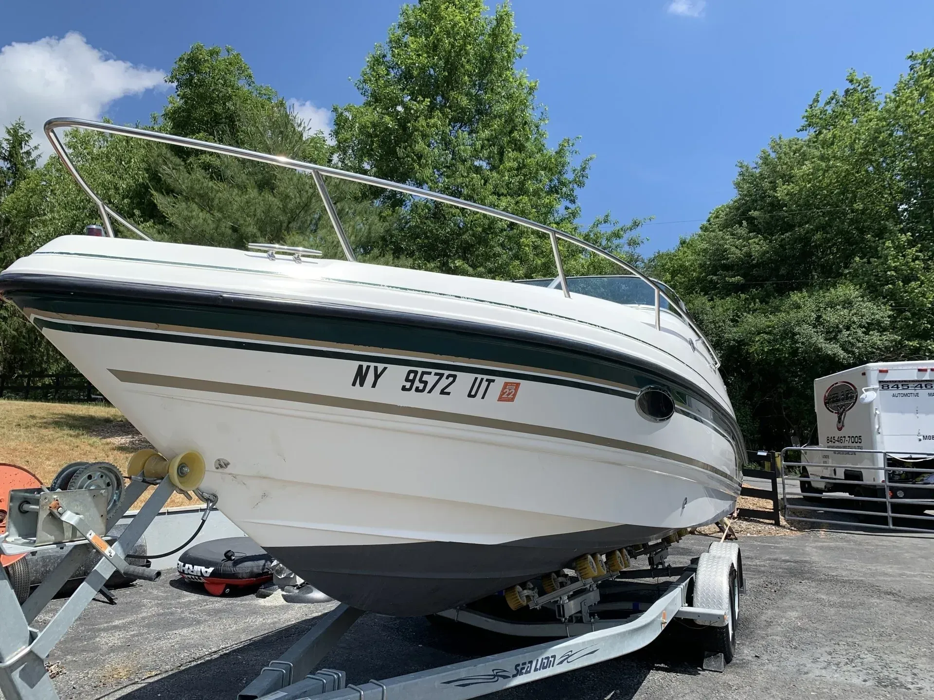 White boat on a trailer outdoors, license plate reads NY 9572 BT.