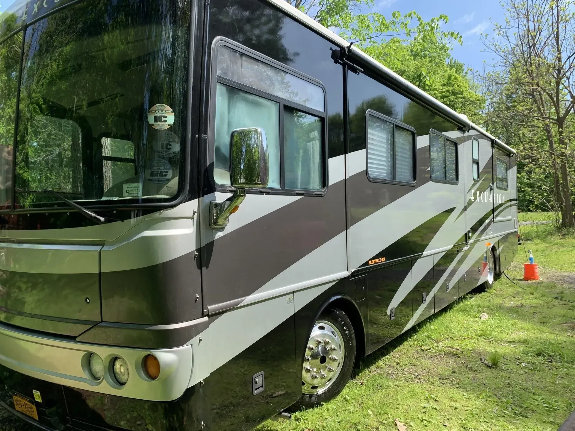 Large, two-tone RV parked on grass; trees in background; sunny day.