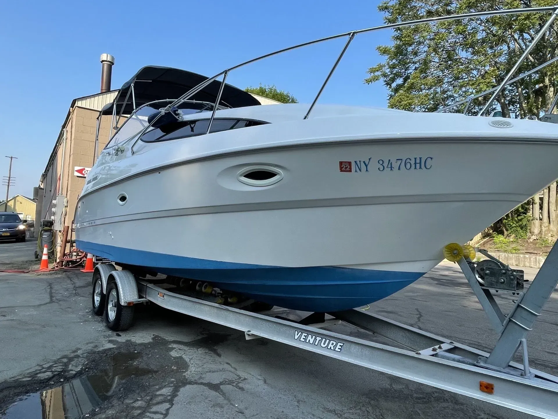 A white and blue boat on a trailer in front of a building on a sunny day.