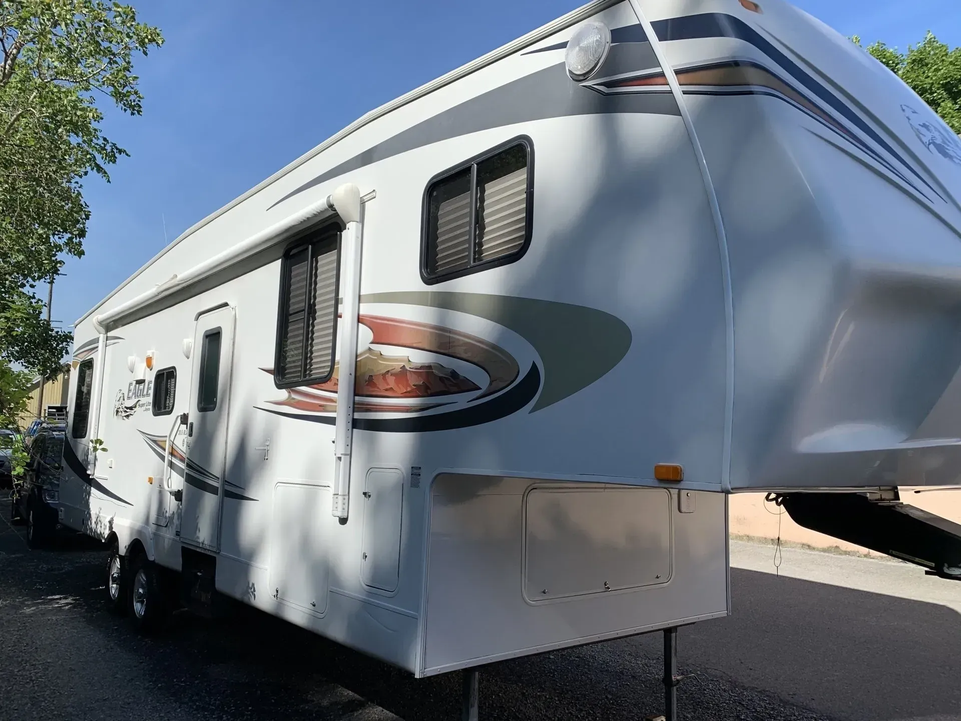 Gray and white fifth-wheel camper parked on a paved street in daylight.