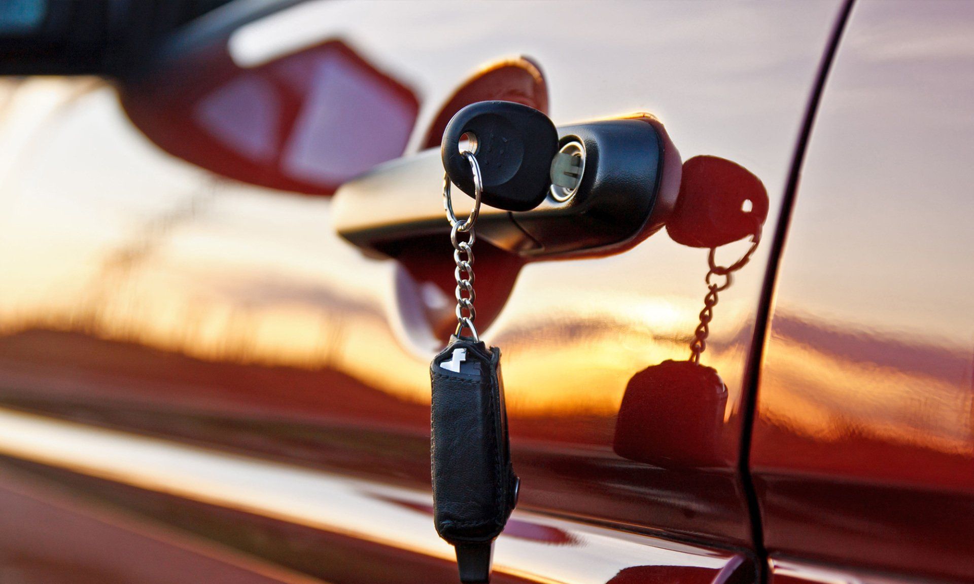 Car door handle with keys in the lock, red car, sunlight.