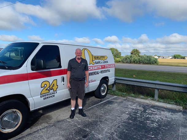 Man stands beside a white van with red stripe and business logo, parked outdoors under a cloudy sky.