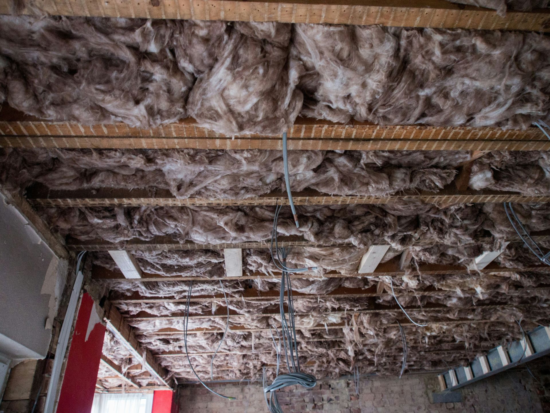 Partially finished room ceiling with exposed insulation, joists, and hanging electrical wiring