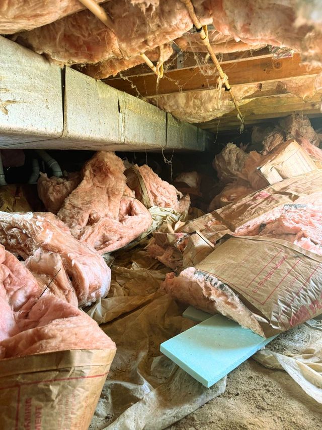 Damaged attic filled with fallen pink insulation and debris under exposed wooden beams