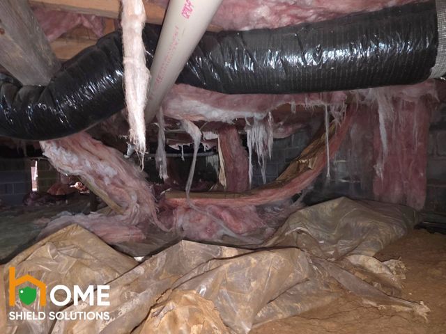 Crawlspace with torn insulation, black ductwork, and plastic sheeting over the floor