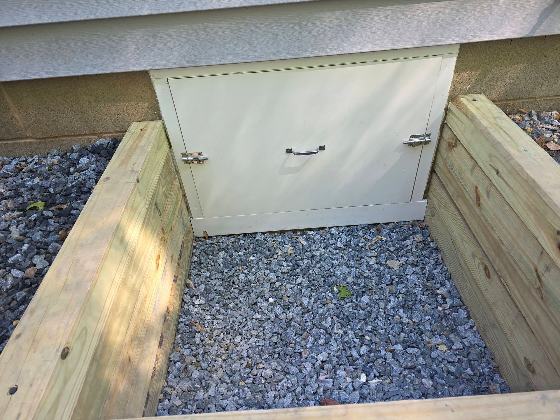Wooden planter box with gravel inside and a small white utility access door on the wall