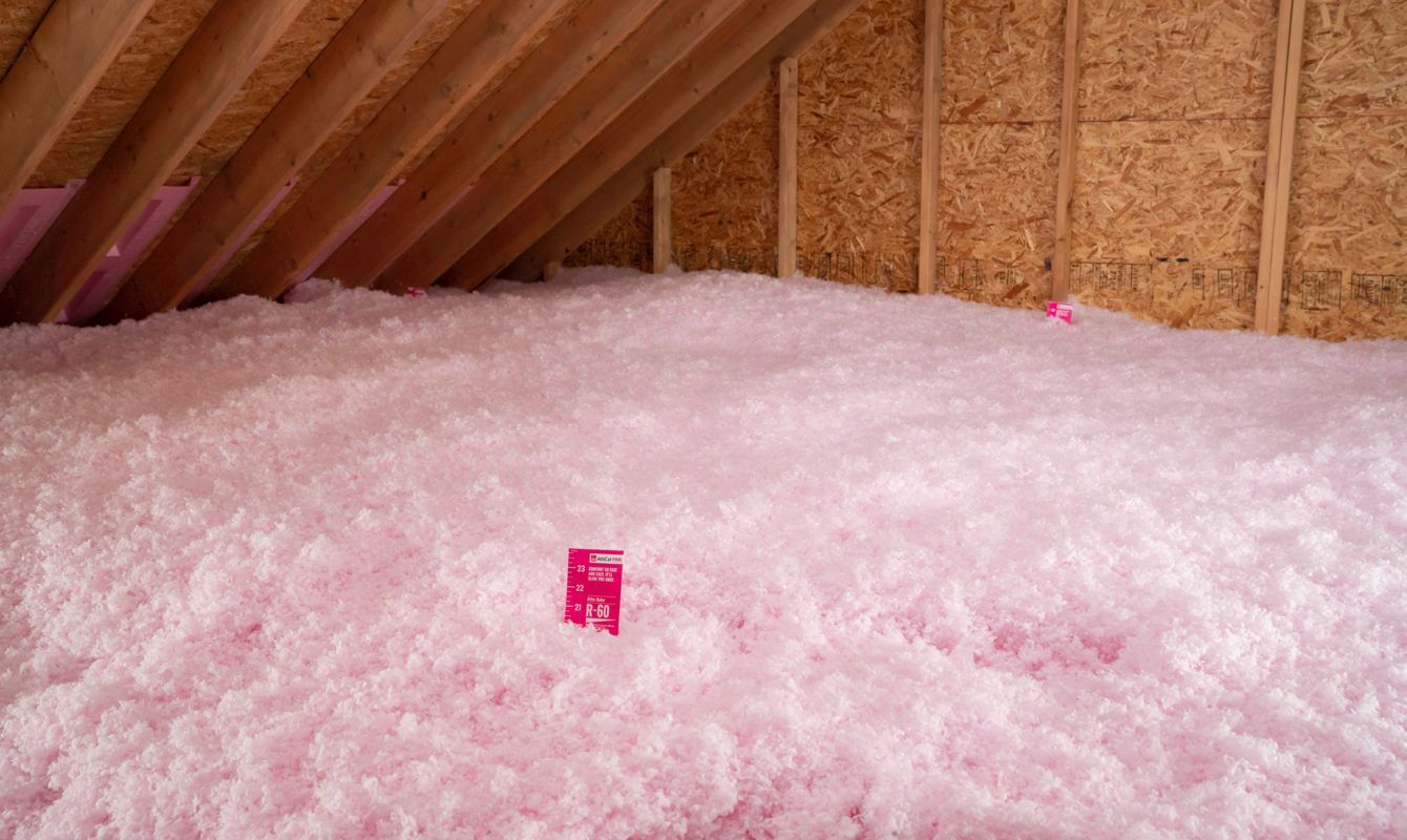 Pink insulation filling an attic beneath exposed wooden rafters