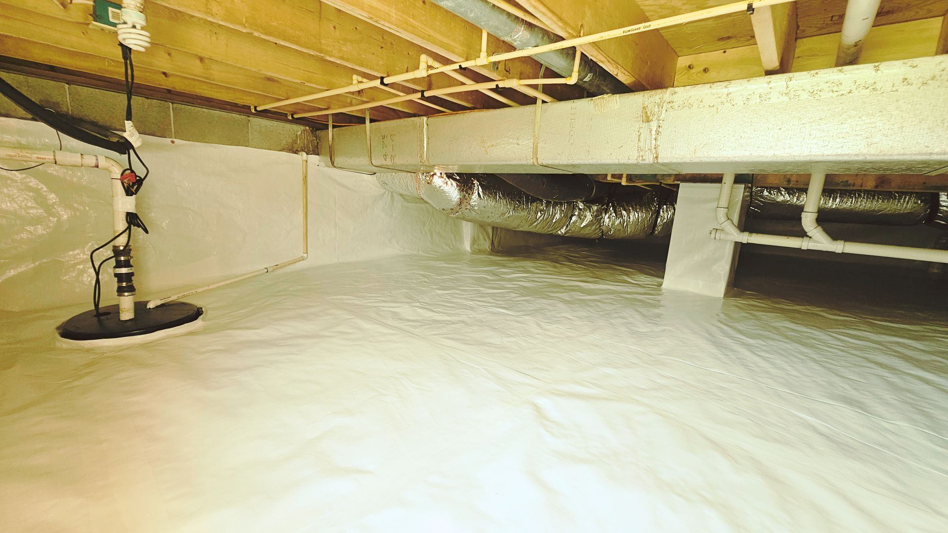 Crawlspace under house with white vapor barrier, exposed beams, and a light on the left.